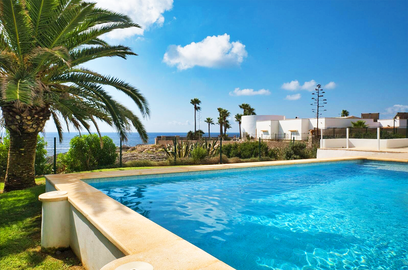 Mediterranean villa swimming pool with palm trees and ocean view on a sunny day.
