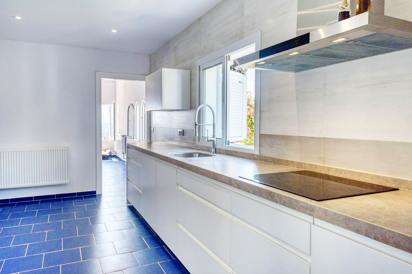 Modern white kitchen with sleek cabinets, stainless appliances, and blue tiled flooring.