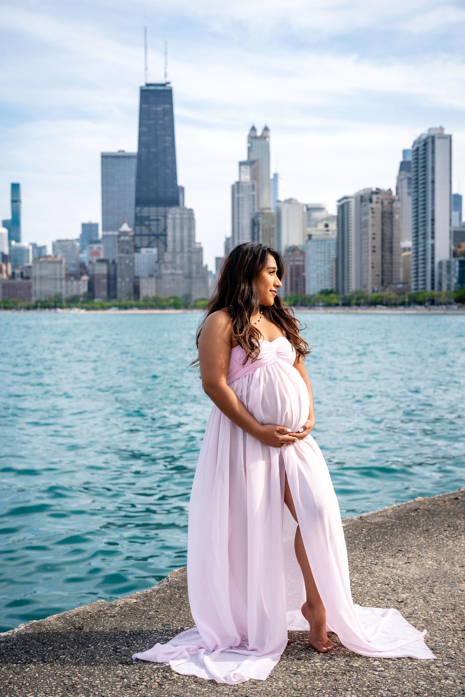 Maternity photos by Chicago skyline with flowing pink dress against Lake Michigan.