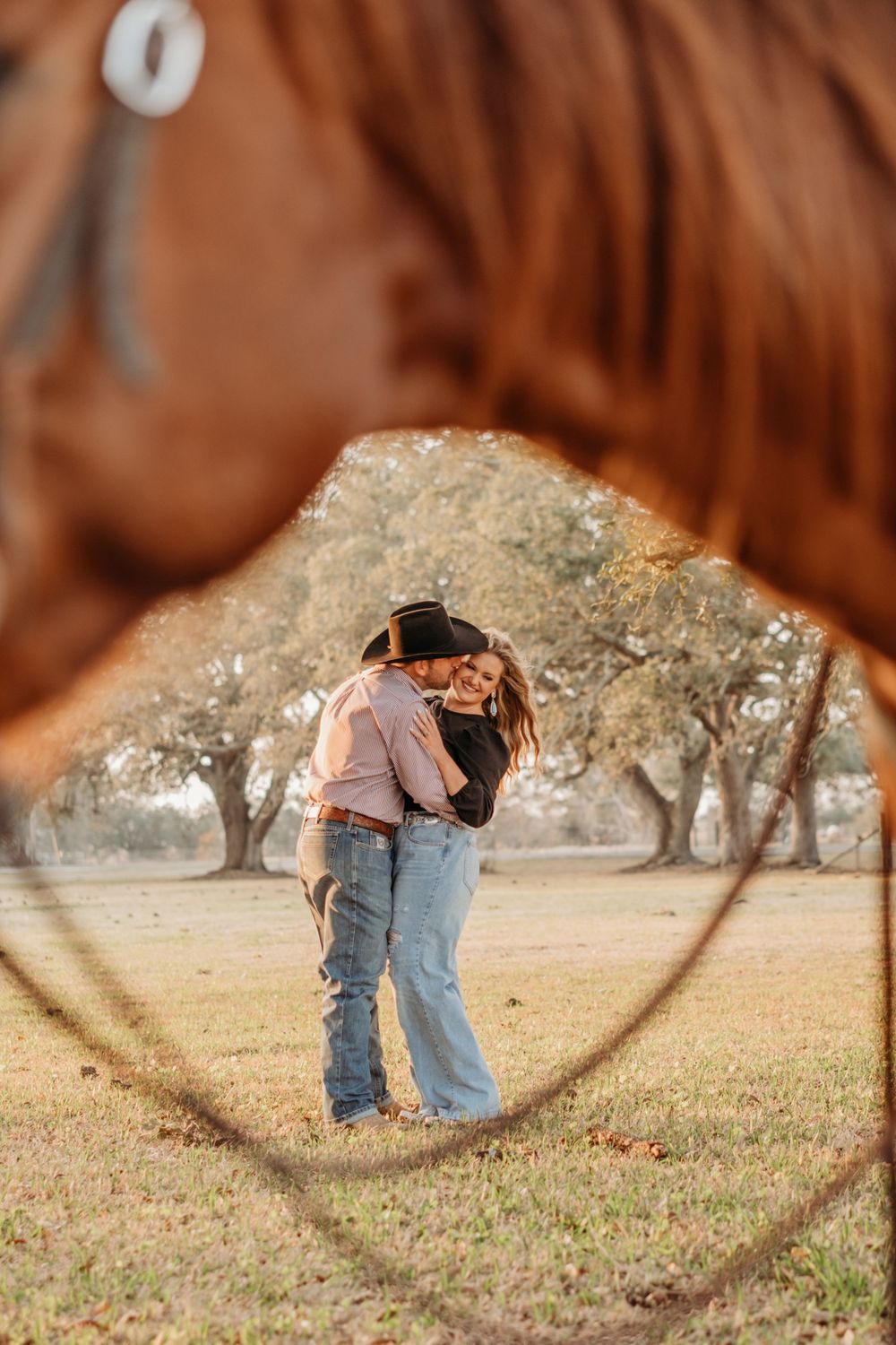 A couple embracing in western attire, viewed through a circular frame against a rural backdrop.