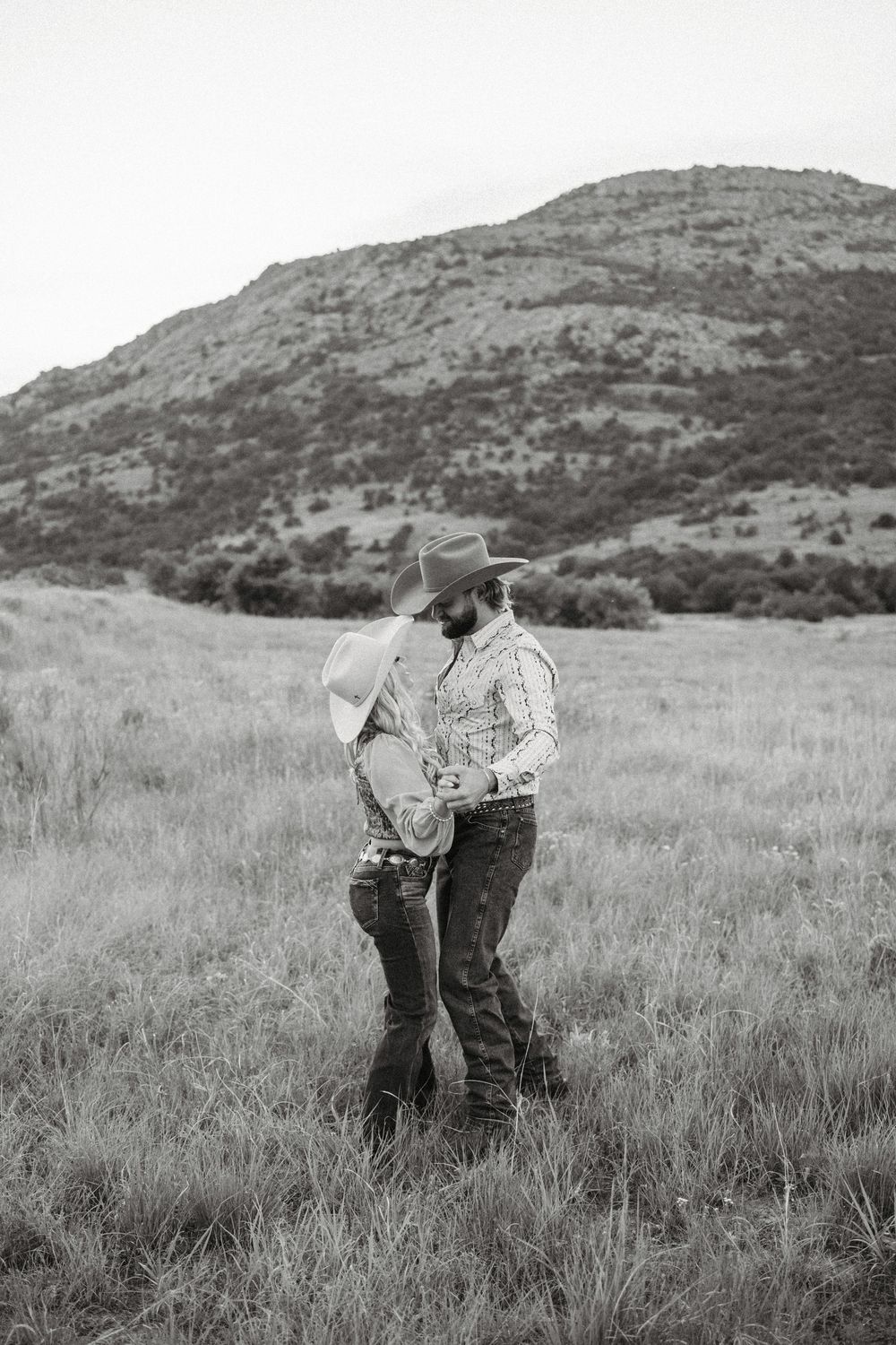 A romantic couple in western wear sharing an intimate moment against a mountainous backdrop.