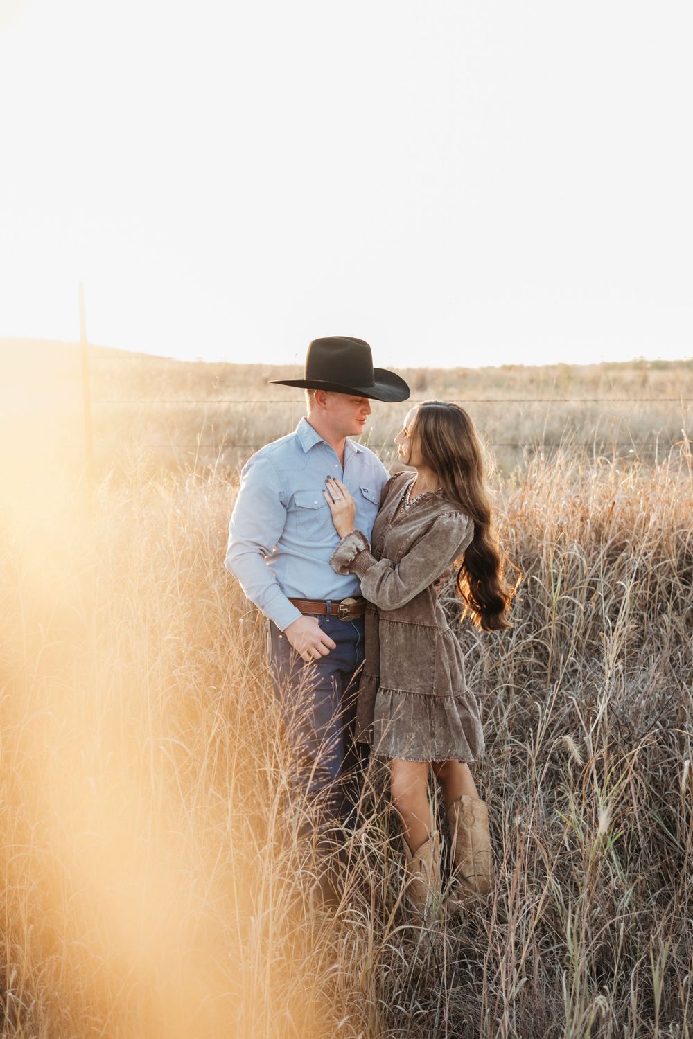 Couple embraces in a golden field of tall grass during sunset.