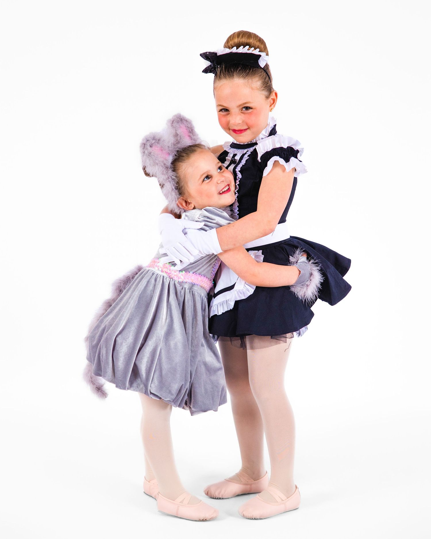 A dancer poses in a gray ballet dress with white floral accents and a tulle skirt against a white background.