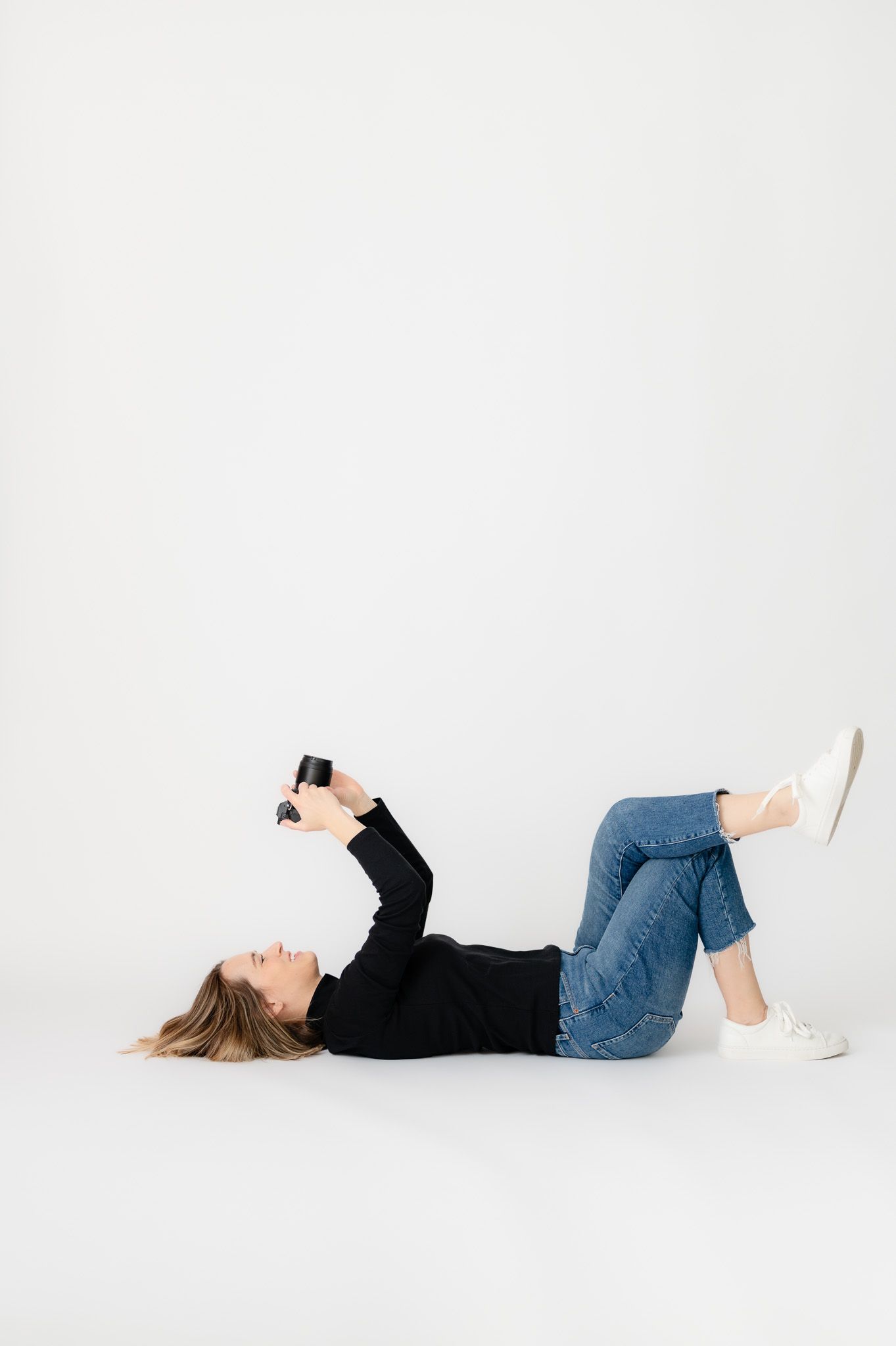 Professional photographer in olive dress holding camera against neutral backdrop.