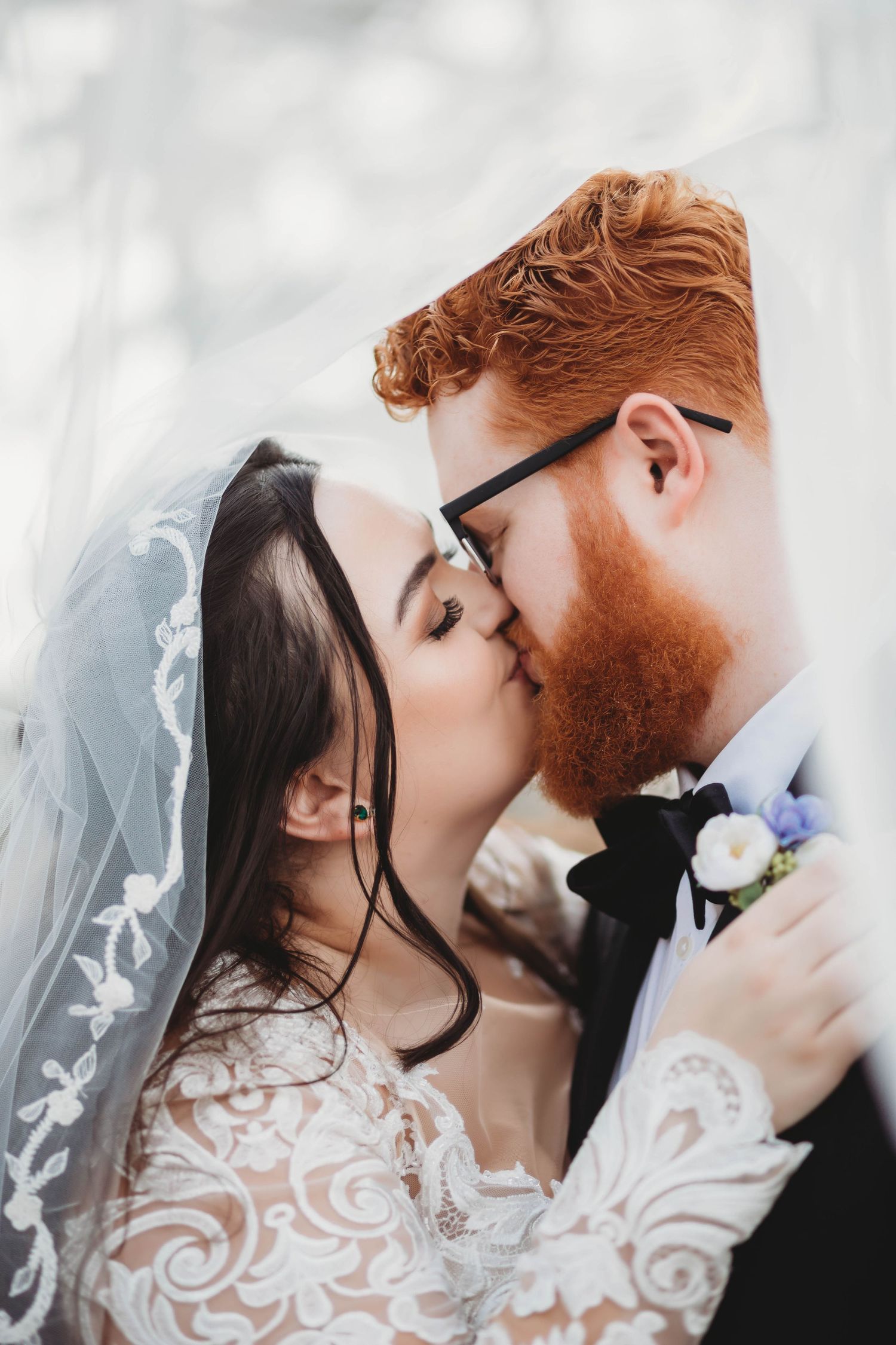 A romantic wedding photograph of newlyweds sharing an intimate kiss under a delicate white lace veil.