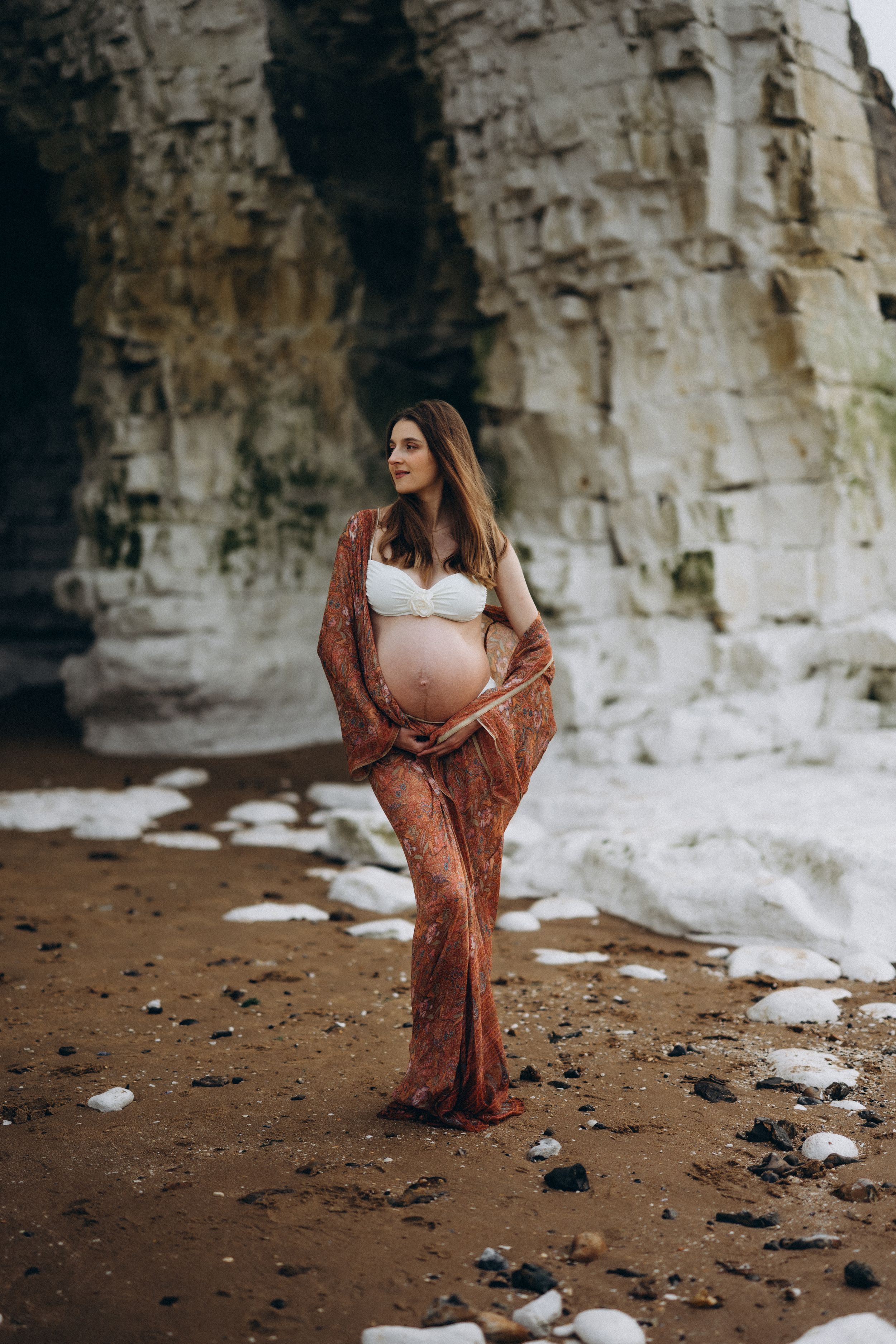 A pregnant woman laying down on the beach during her maternity photo session with Forever Ours Photography in Botany Bay, kent