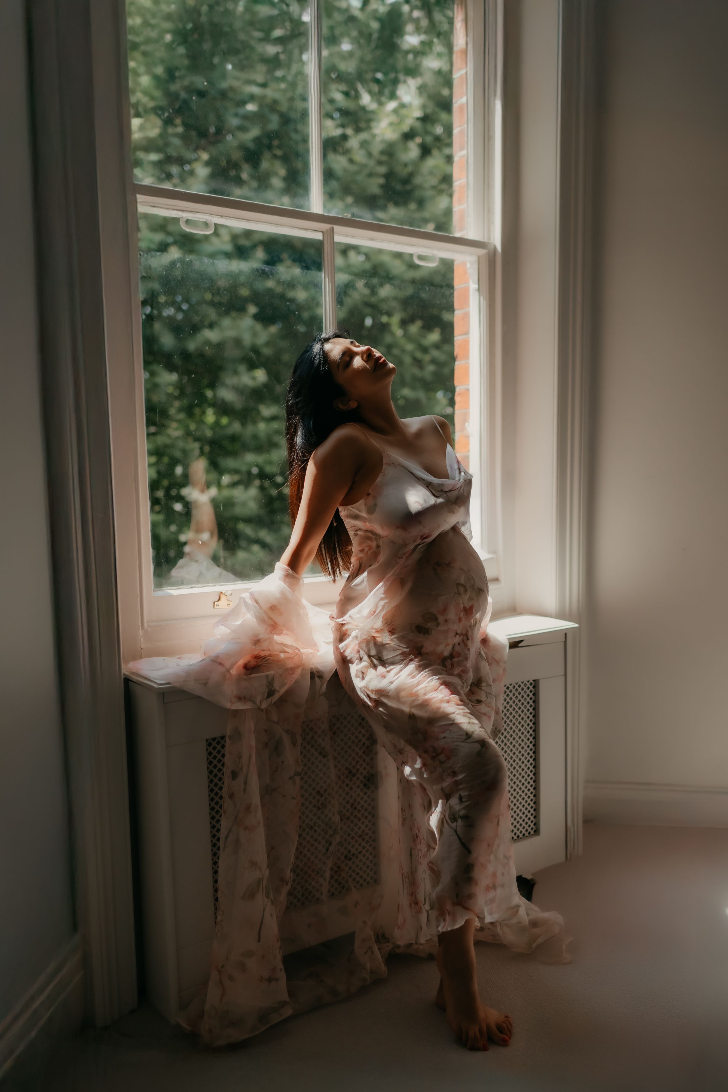 a pregnant woman leaning back with her hands on the window sill