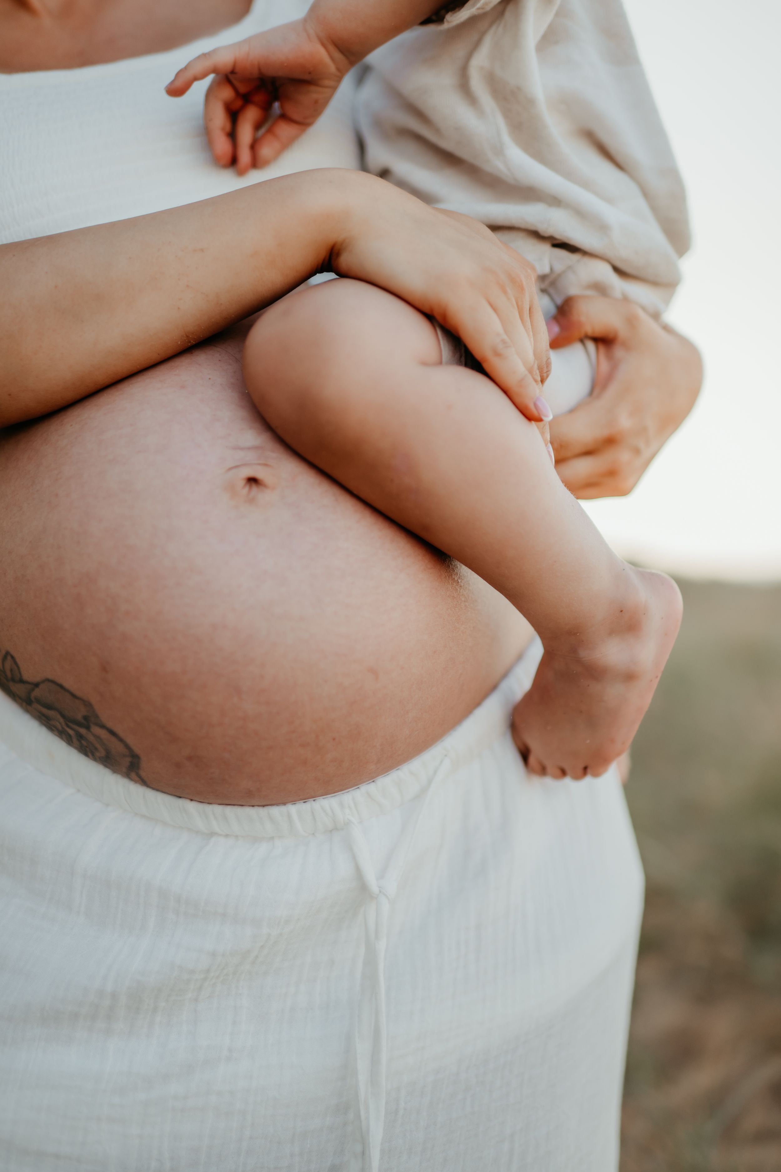 A close-up of a mother's pregnant belly, holding her young toddler in her arms, kent family photographer