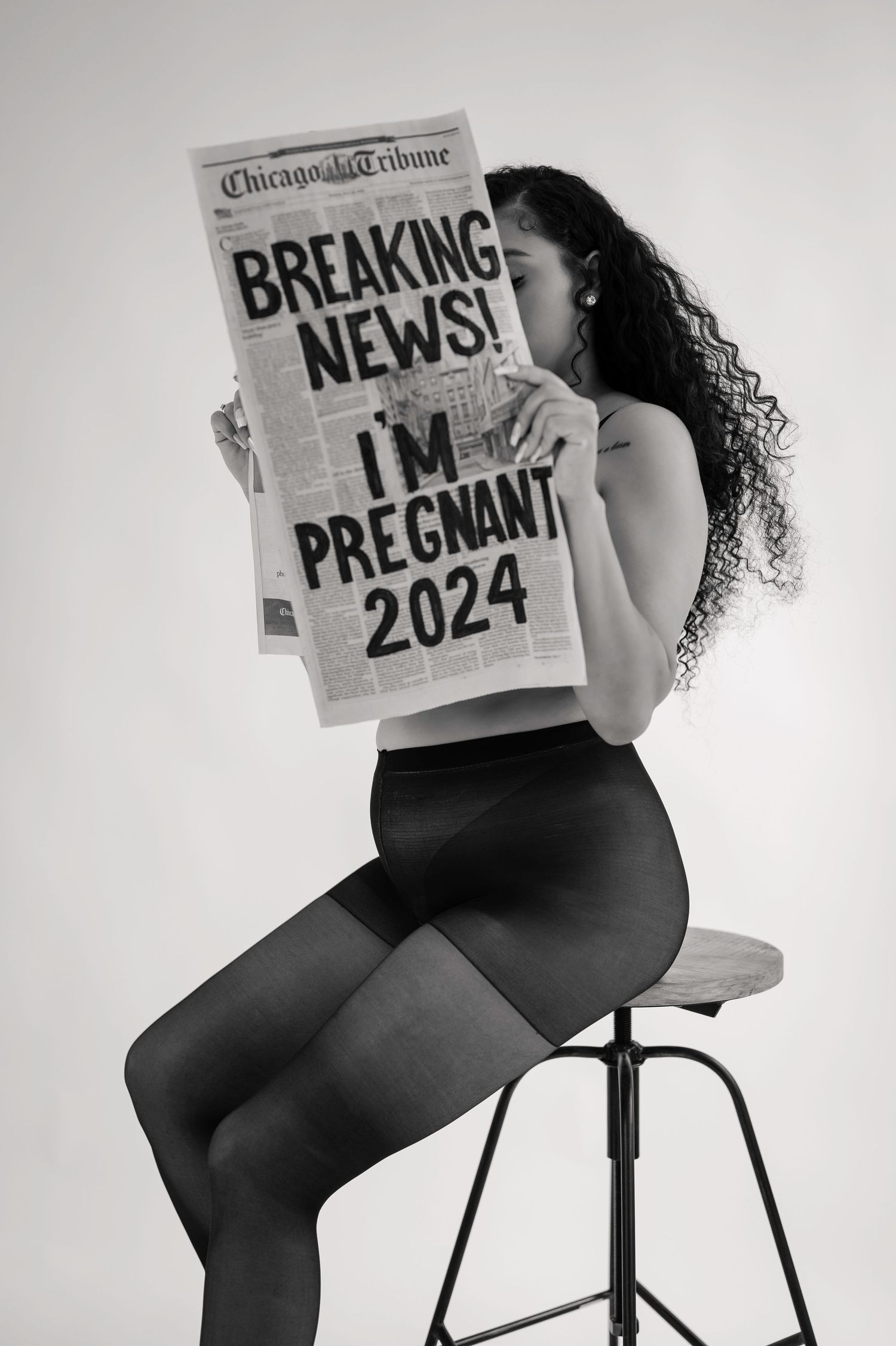 Creative pregnancy announcement photoshoot with newspaper props in black and white.