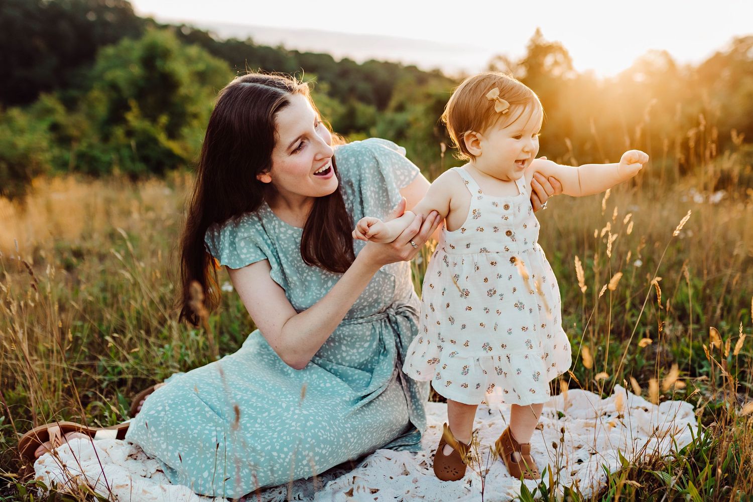 Mother and child sitting on blanket in golden sunset meadow.