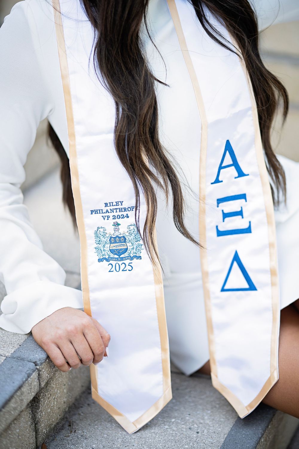 White graduation stole with blue Alpha Xi Delta Greek letters and embroidered Class of 2023 crest.