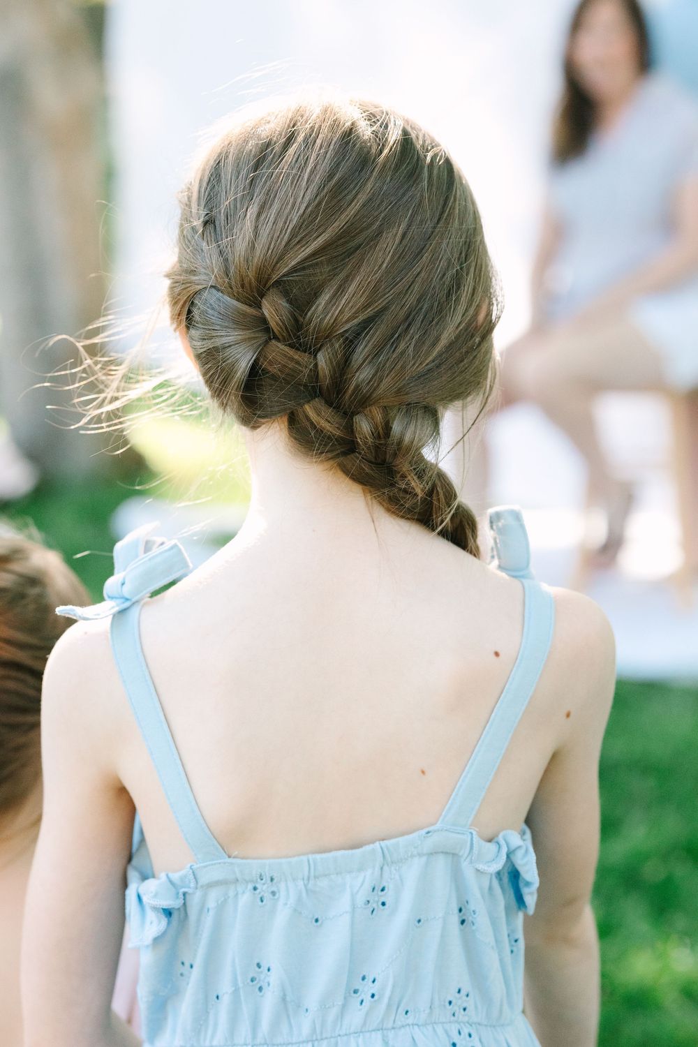 Back view of braided hair and blue summer dress against green background.