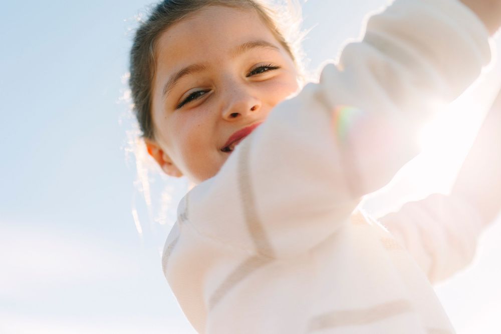 A child in white clothing reaches upward against a bright, airy background.