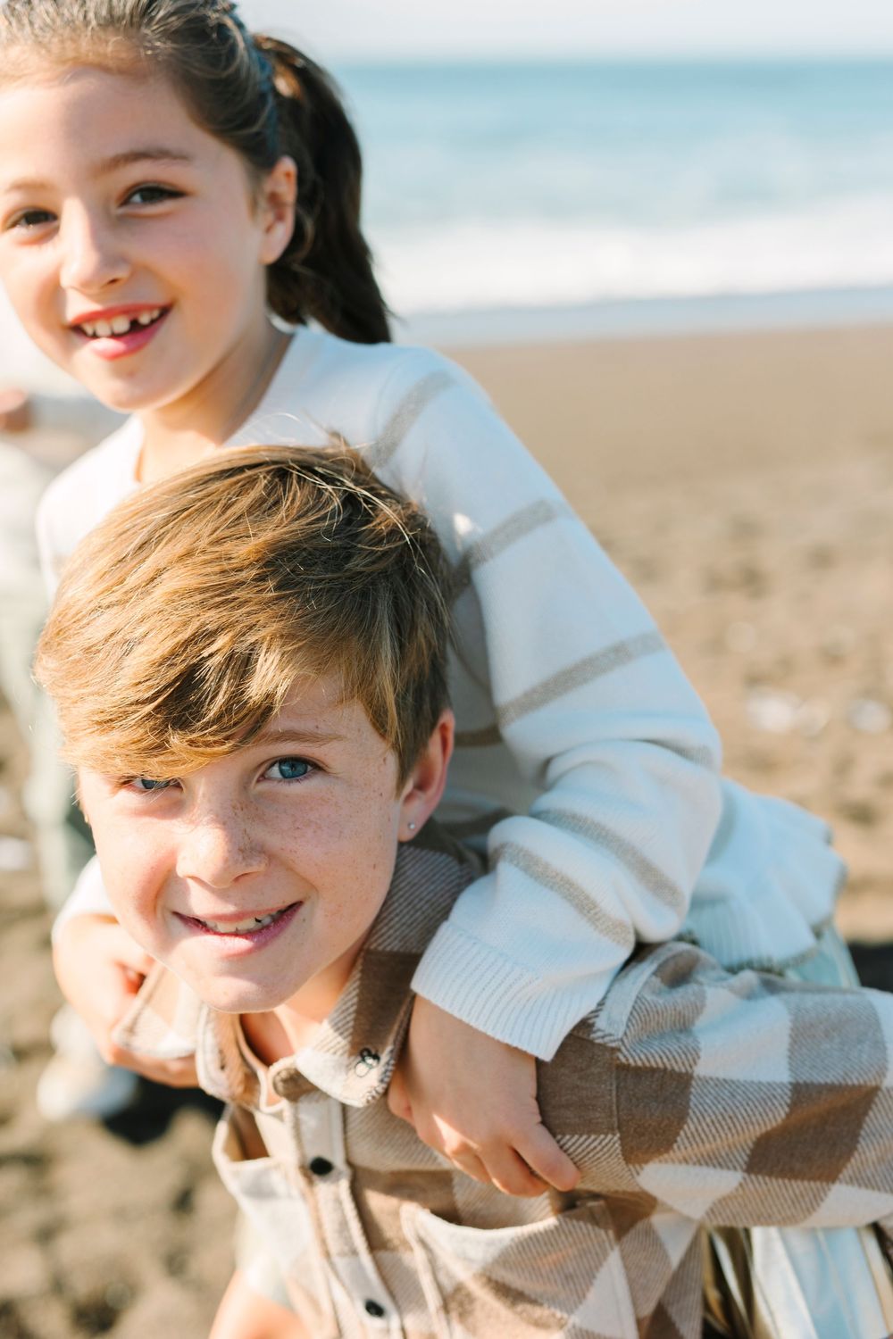Playful candid moments captured at the beach with soft natural lighting and joyful expressions.