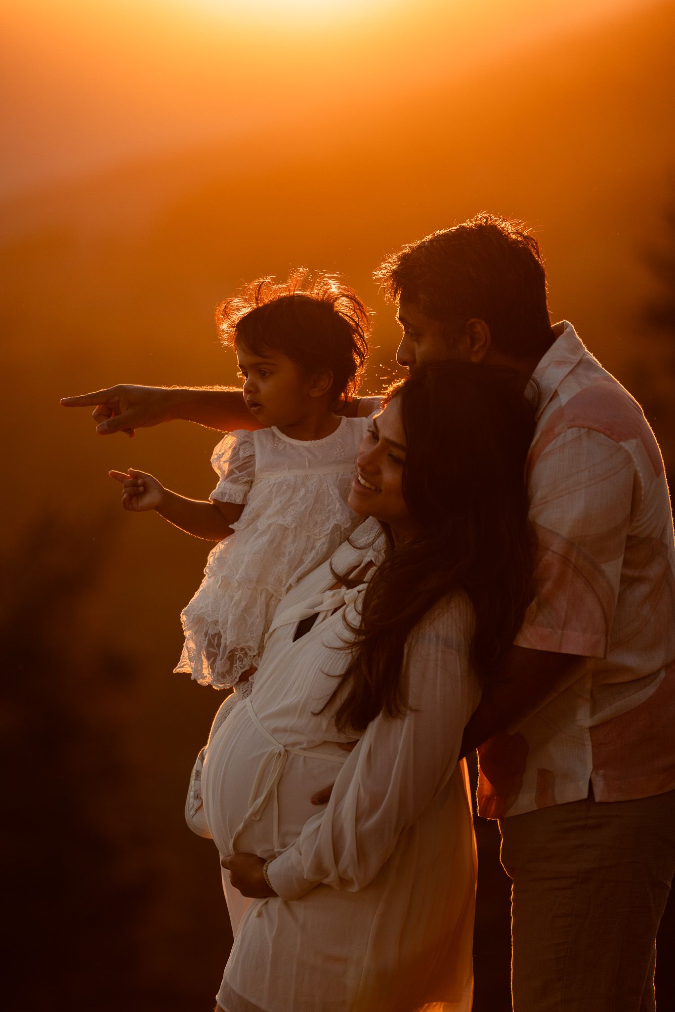 Family silhouetted against orange sunset sky pointing at the horizon.