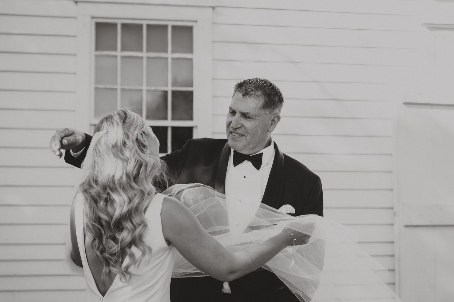 Black and white photo of a couple sharing their first dance outside a white building.