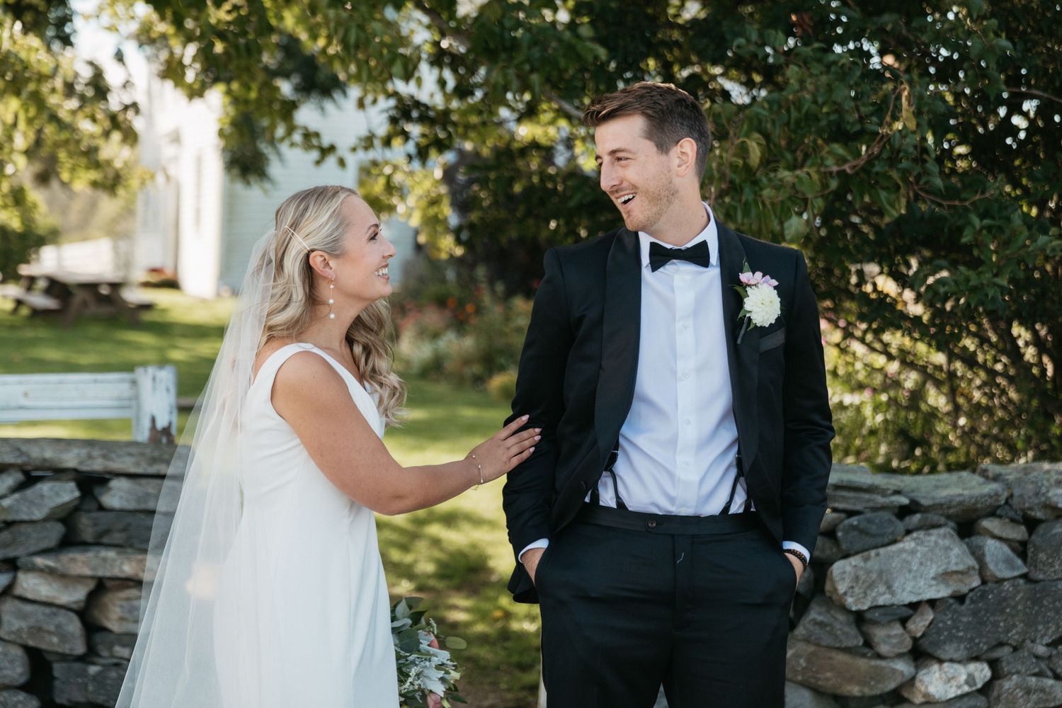 Candid moment between newlyweds on garden path with rustic stone wall.