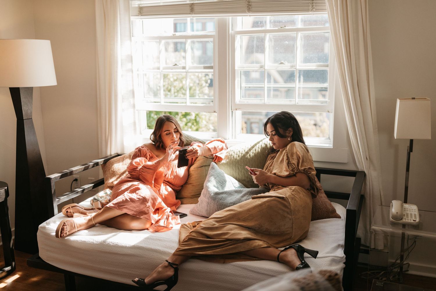 Two friends enjoying a casual morning lounging in bed with coffee and conversation.