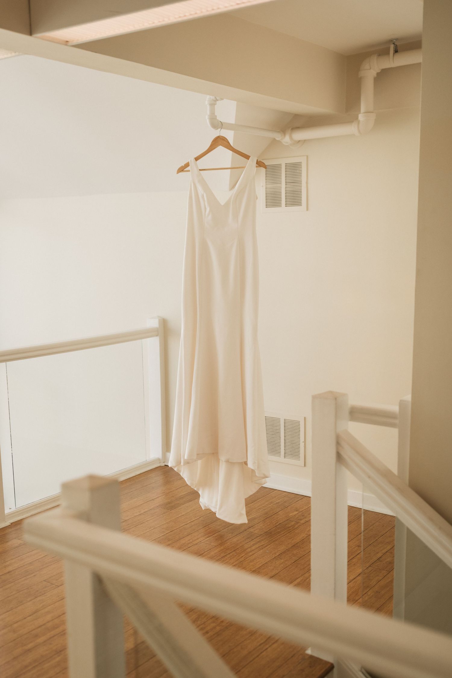 Elegant white wedding dress hanging on a wooden hanger in a bright, minimalist room.