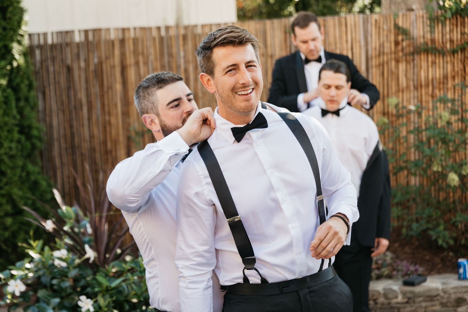 Groomsmen in suspenders and bowties sharing laughs before the wedding ceremony.