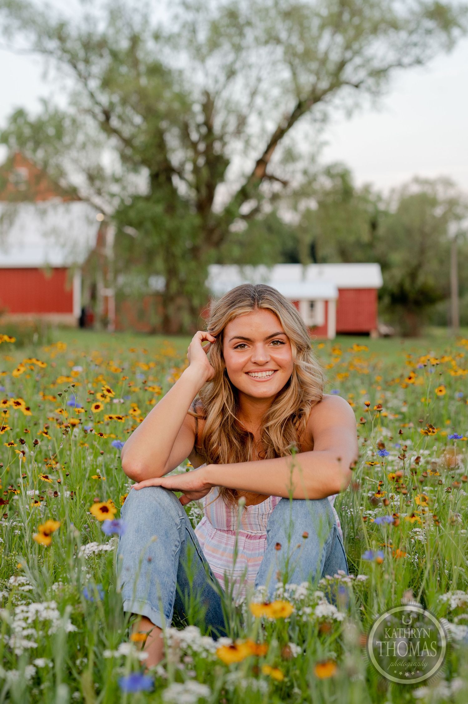 Rustic outdoor portrait with red barns and blooming wildflowers in the background.
