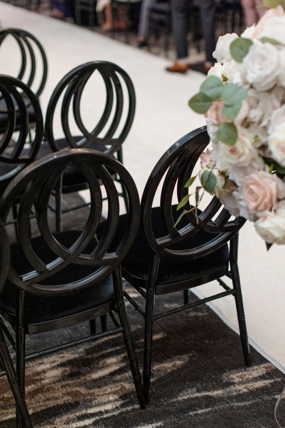 Black circular-back chairs arranged with white floral arrangements at an elegant wedding ceremony setup.