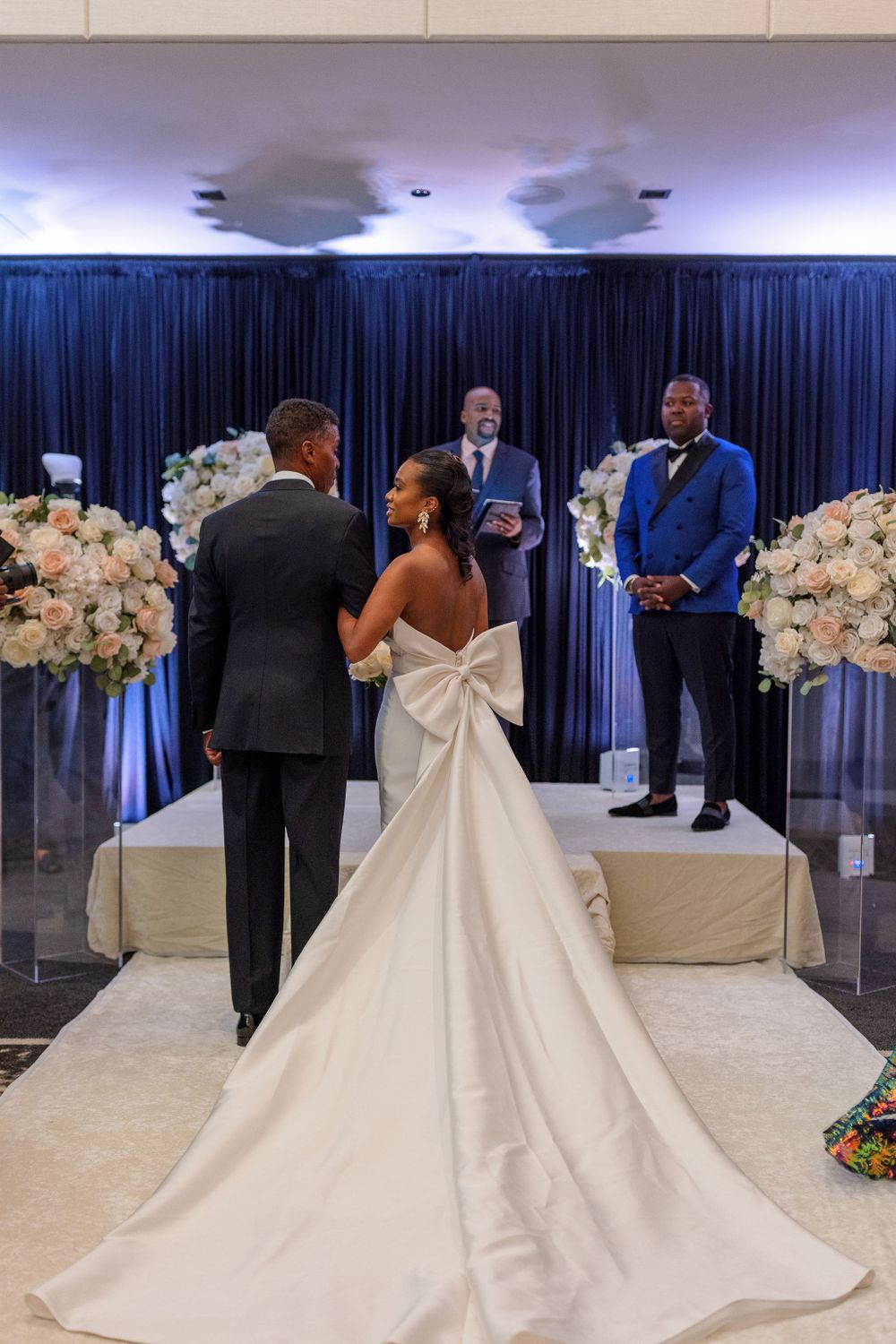 A wedding ceremony setup with navy blue curtains and white floral arrangements framing the altar.