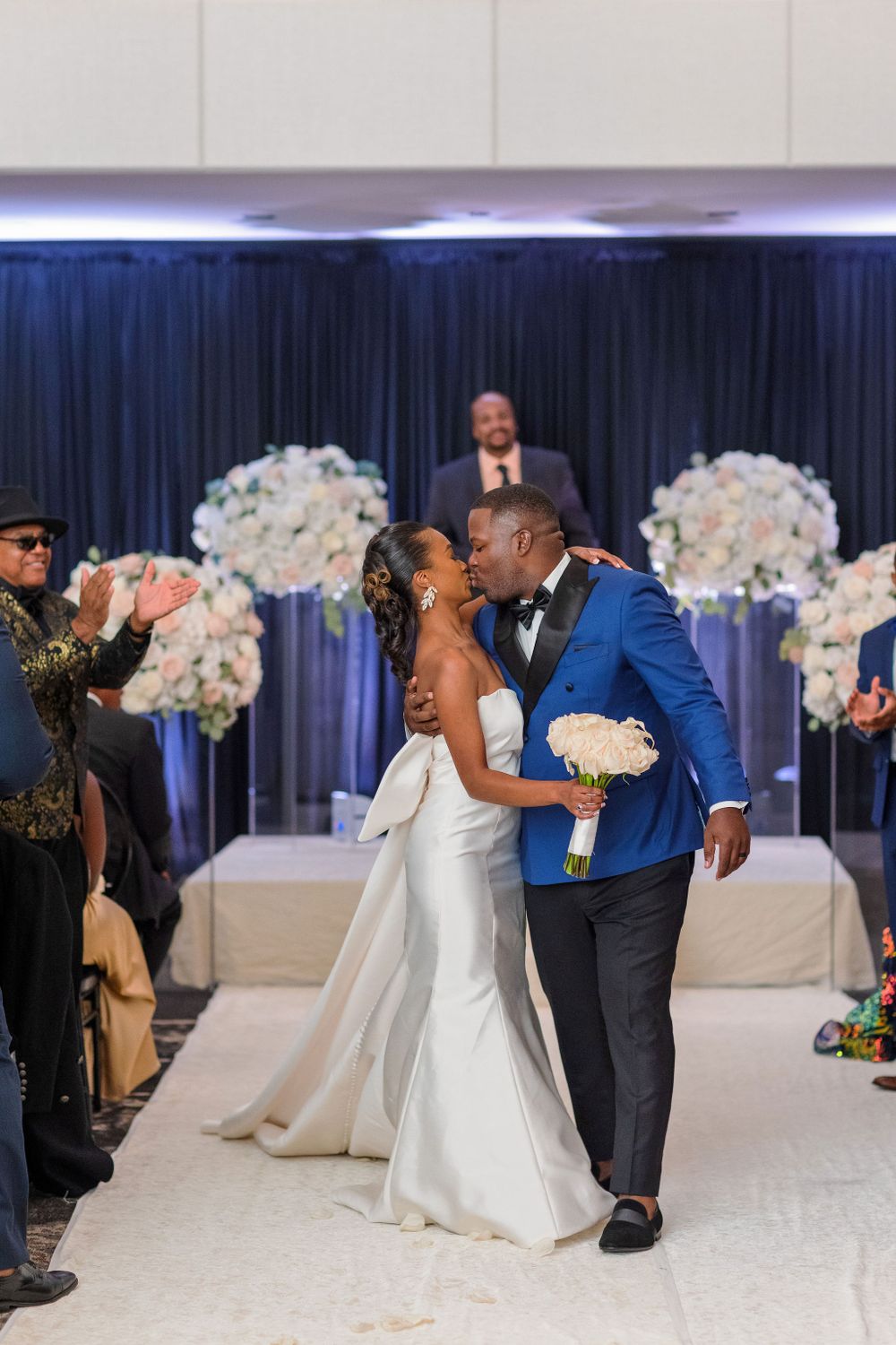 A couple celebrates during their recessional walk with elegant white floral arrangements and blue draping.