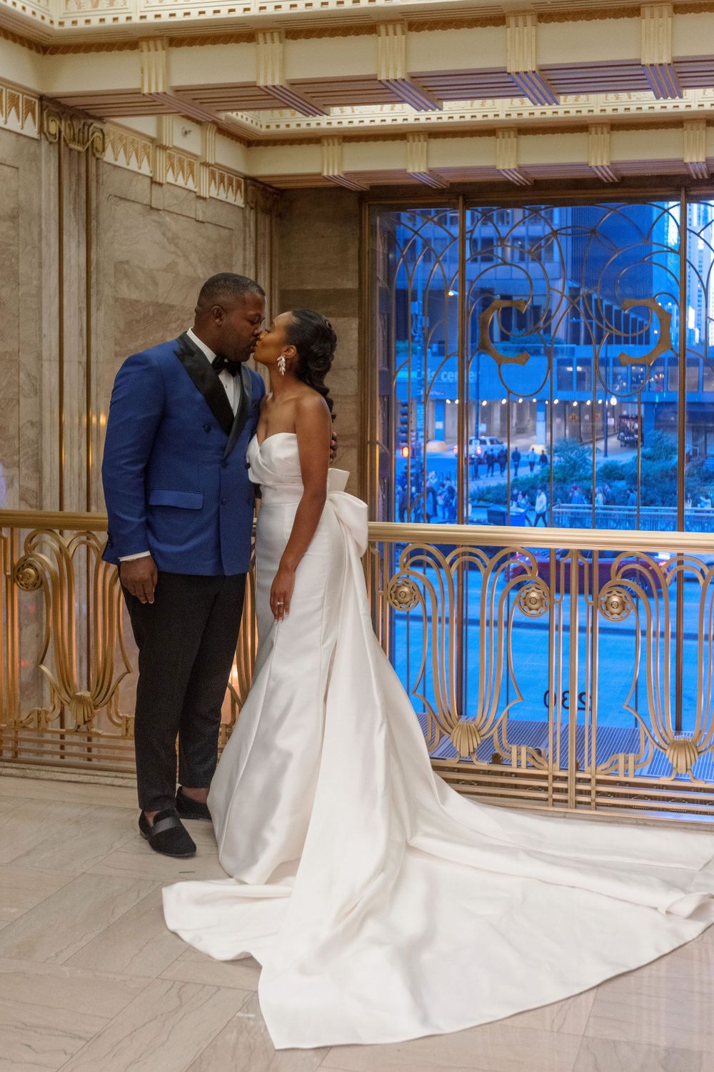 A couple shares a romantic moment in front of an ornate blue-lit window display at their wedding venue.