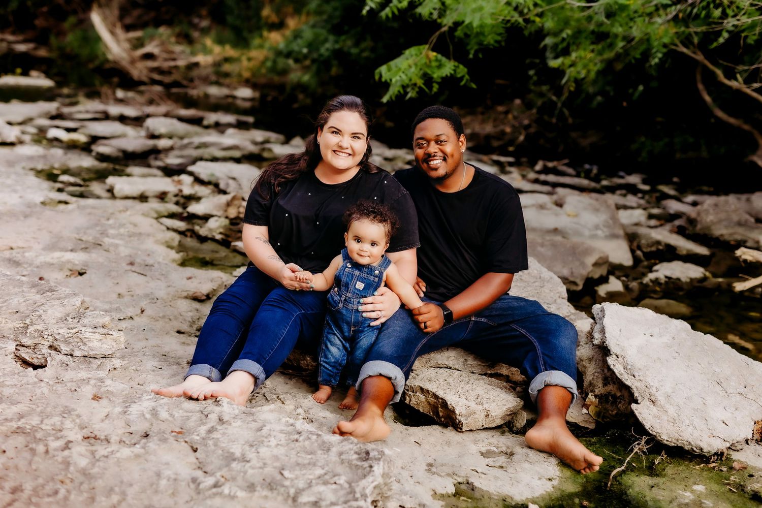 Family sitting together on rocky terrain by a stream.