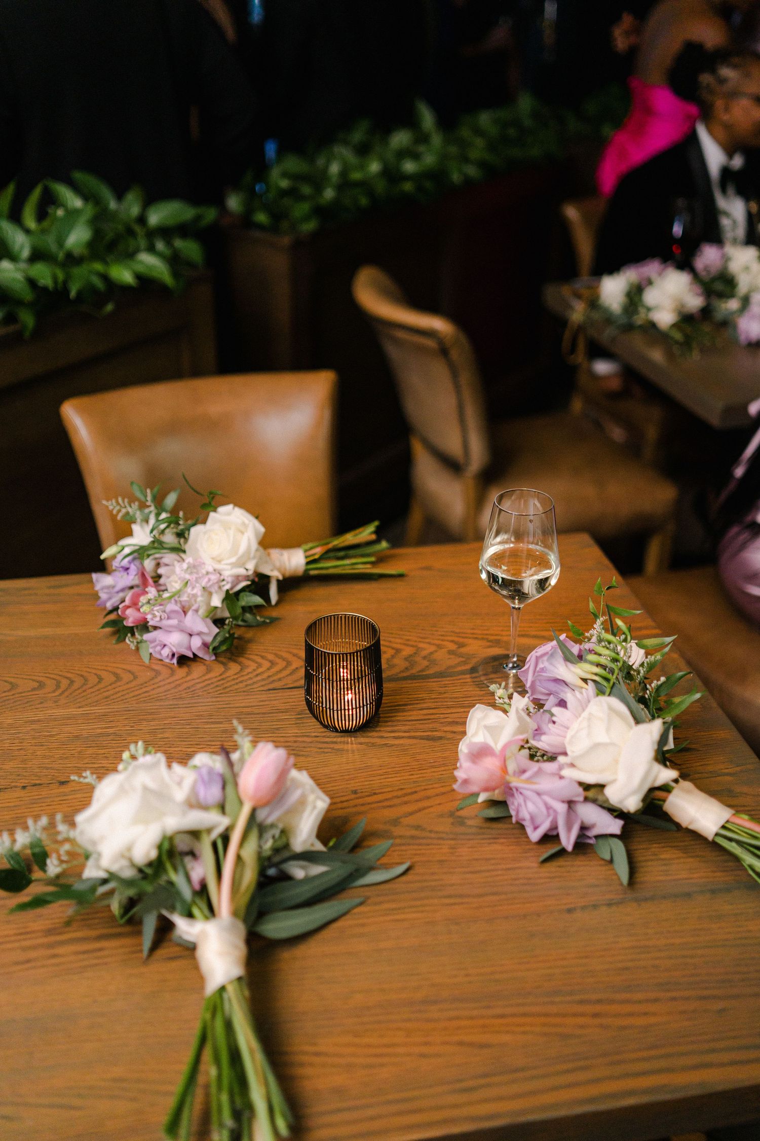 Floral bouquets with purple and white flowers on wooden table with wine glass.