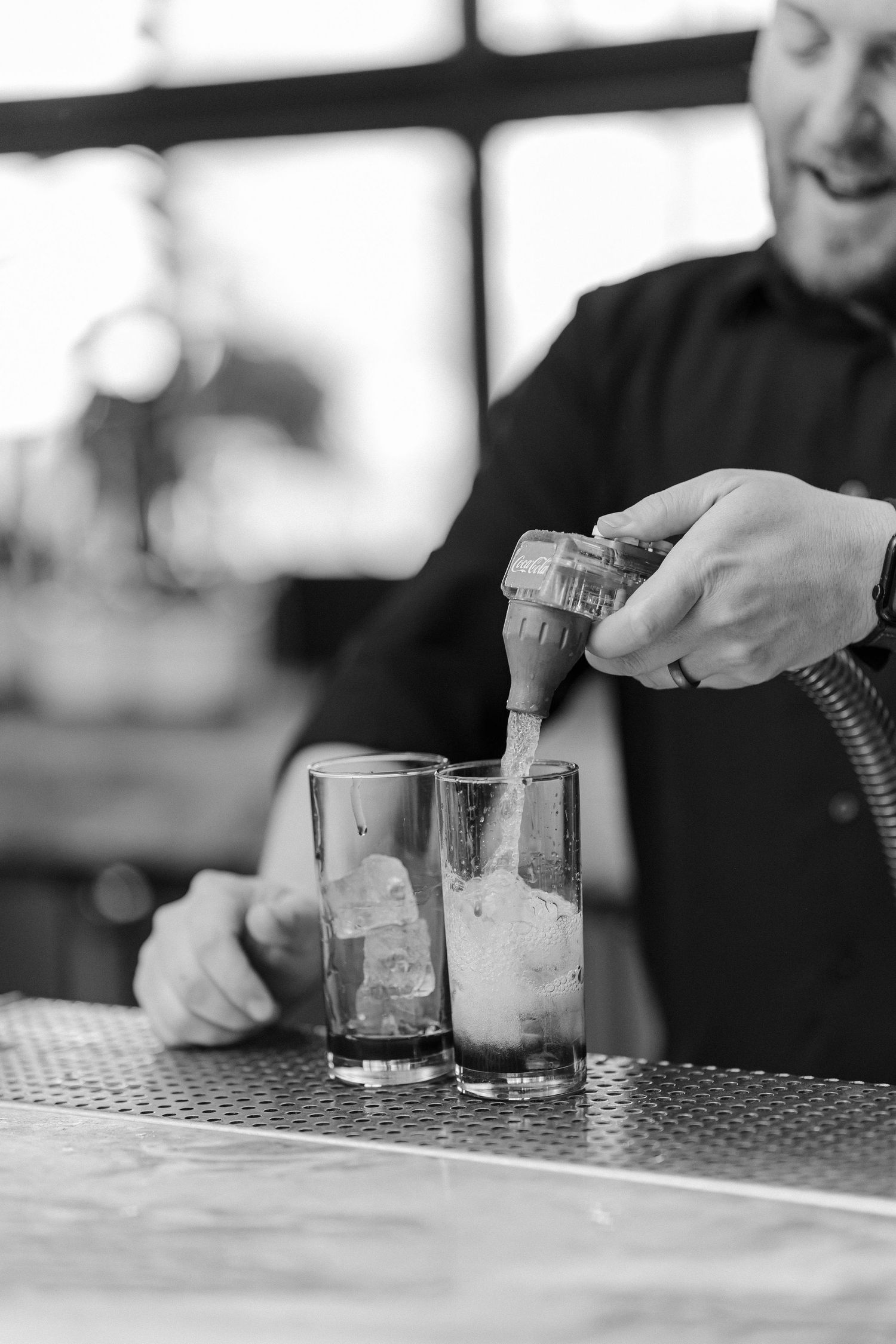Bartender pouring drinks into ice-filled glasses at bar.