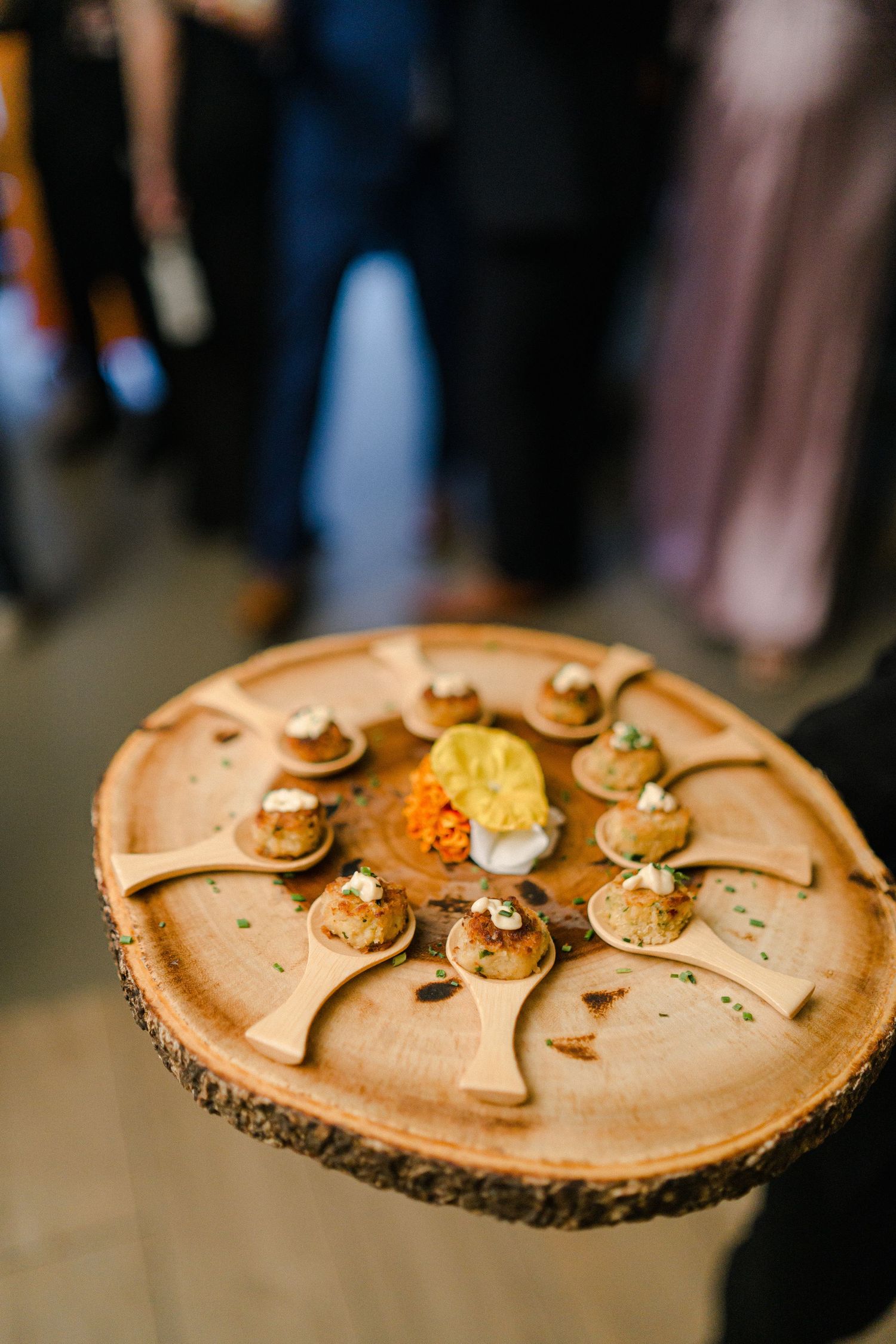 Appetizers arranged on circular wooden serving platter at event.