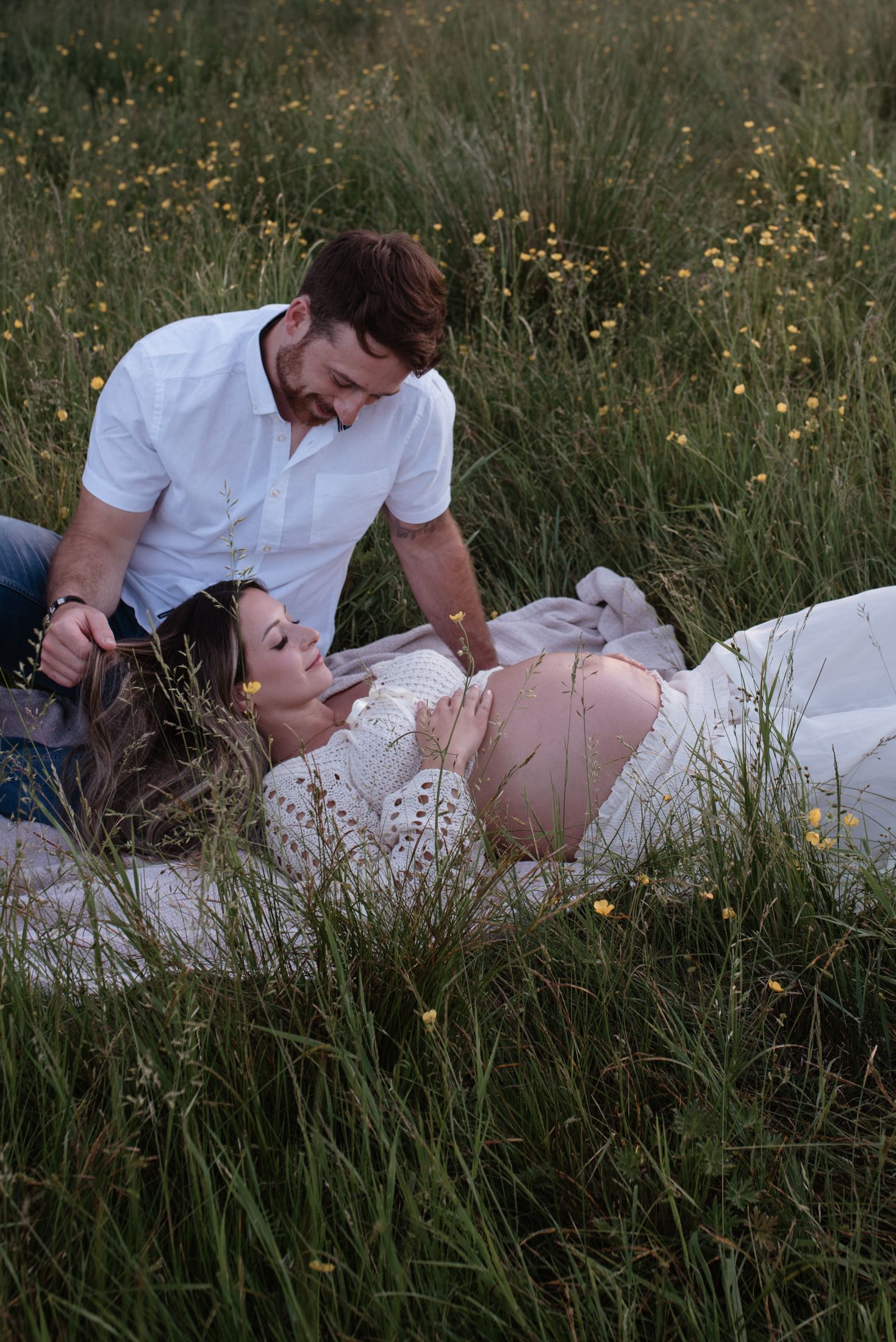 Intimate maternity photoshoot in tall grass field at sunset.