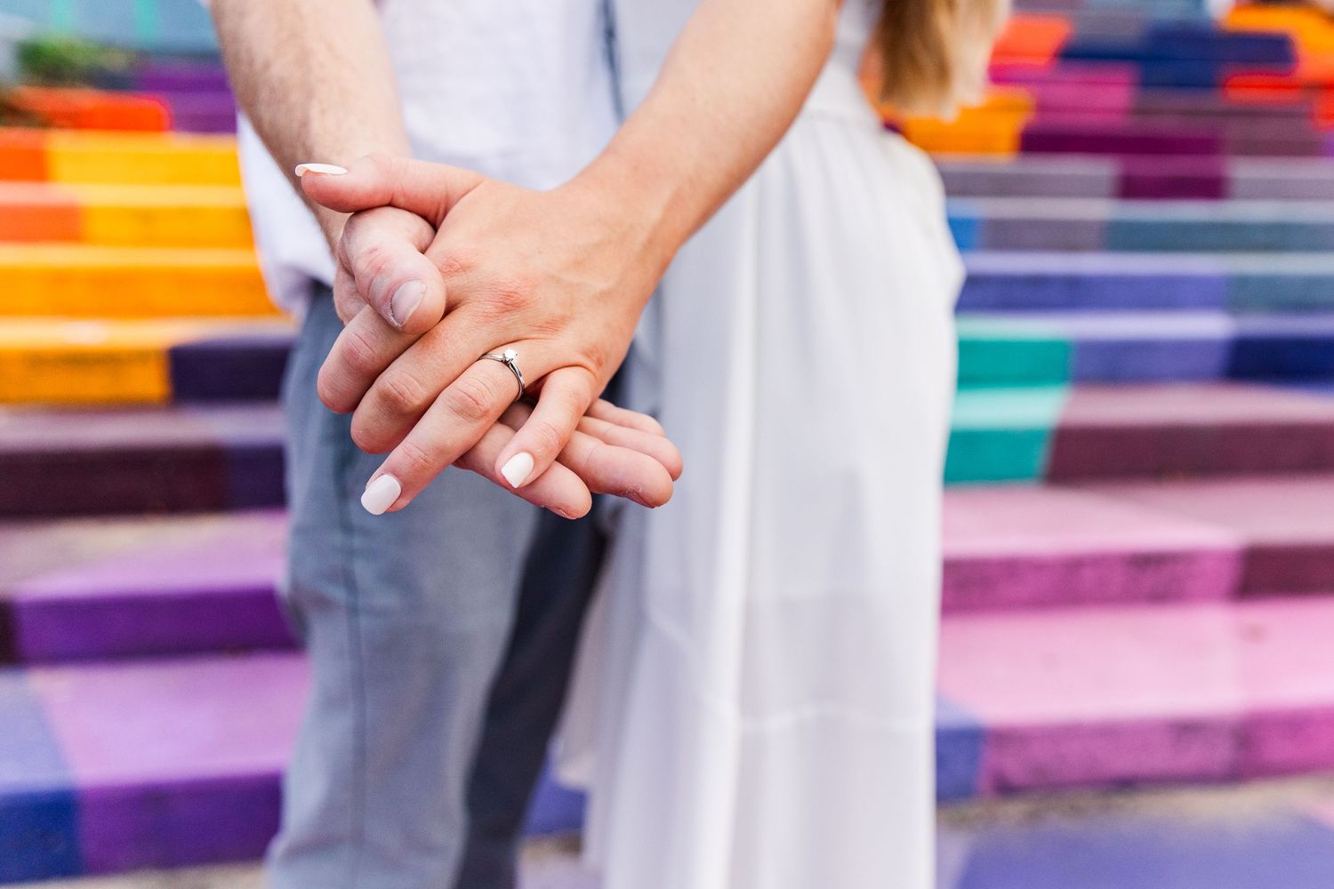 Close-up of intertwined hands against colorful rainbow stairs background.