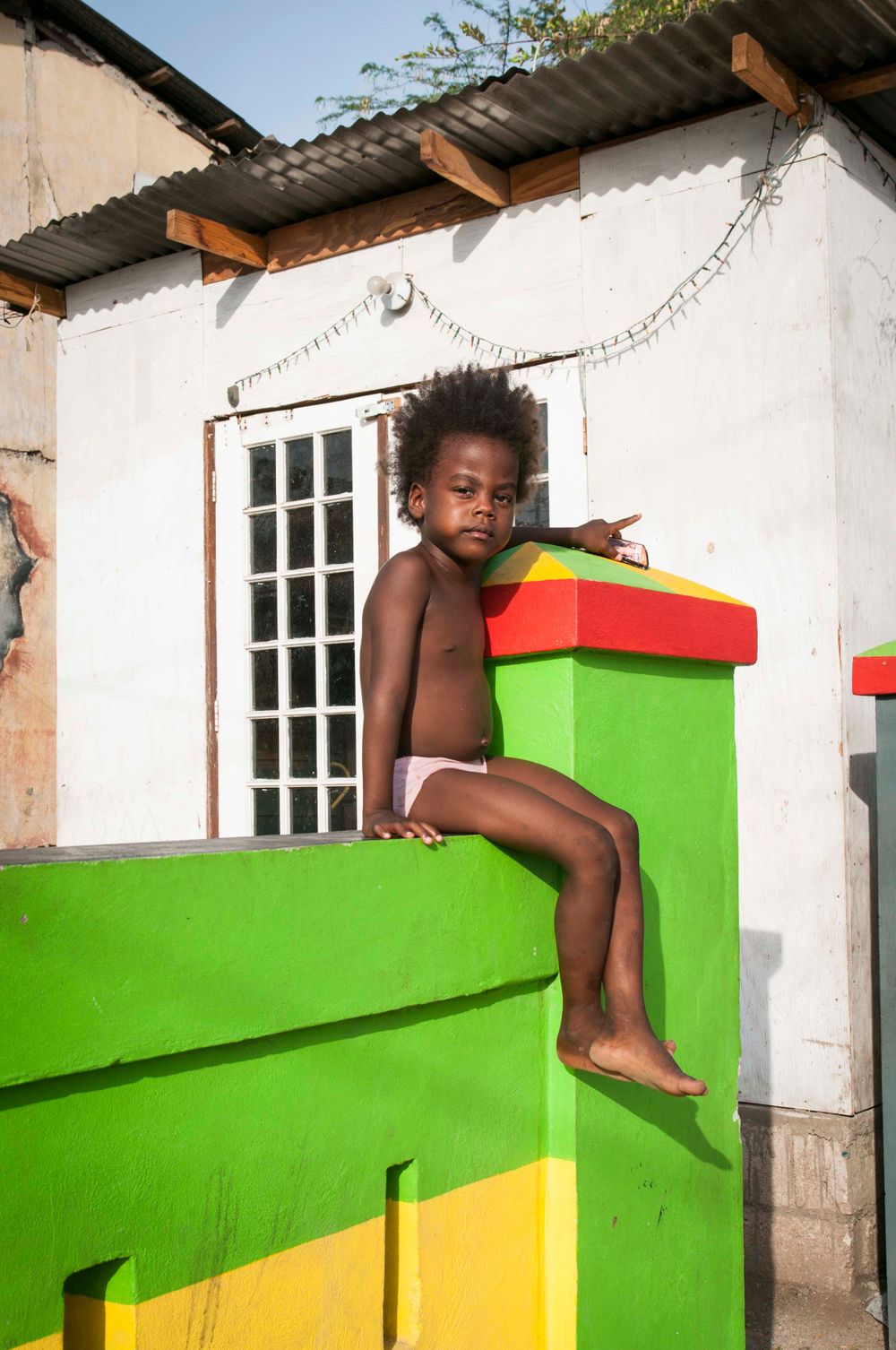 Child sitting playfully on a colorful green and yellow painted wall structure.