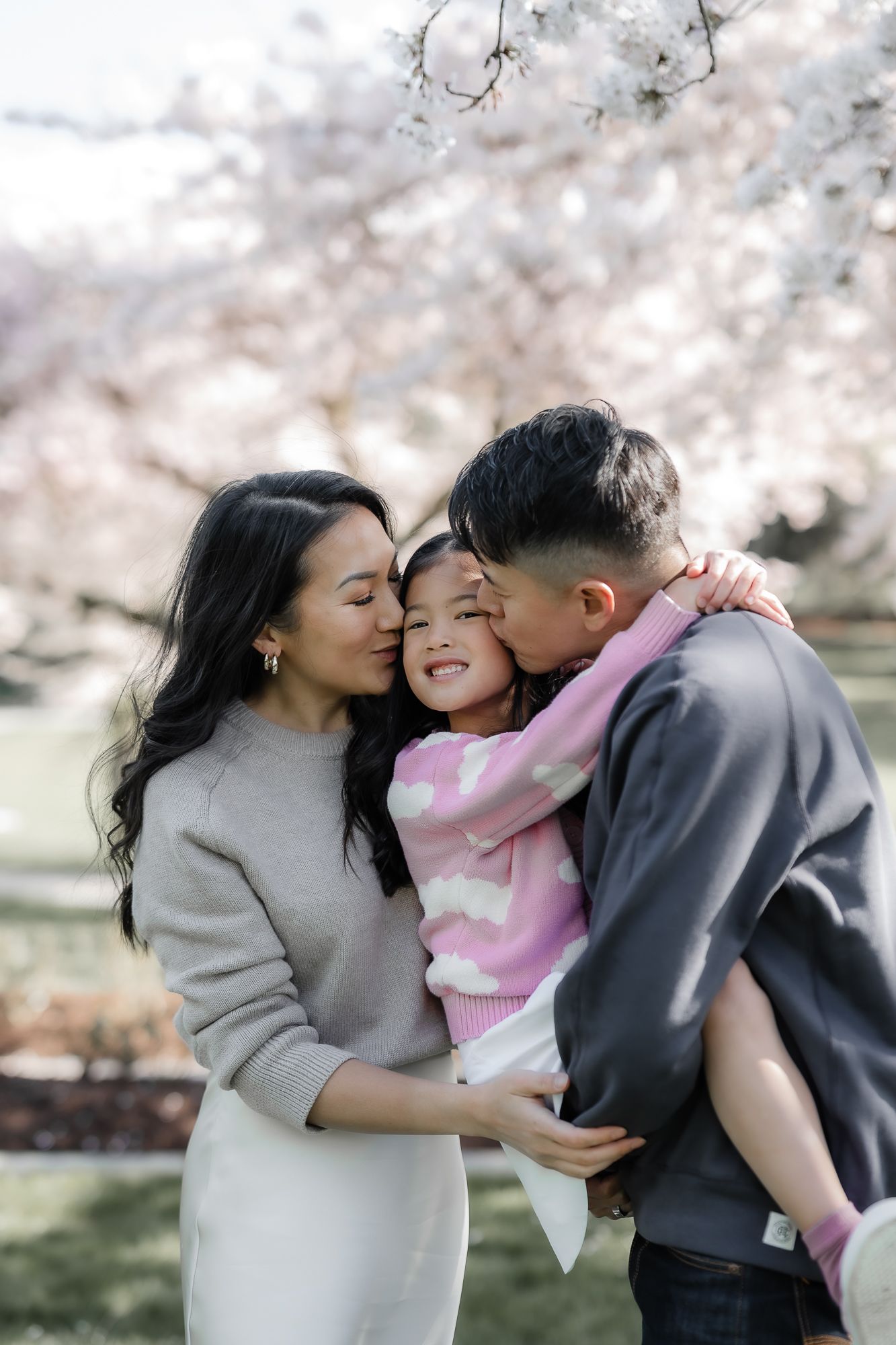 A happy family embraces outdoors during cherry blossom season with beautiful pink blooms in the background.