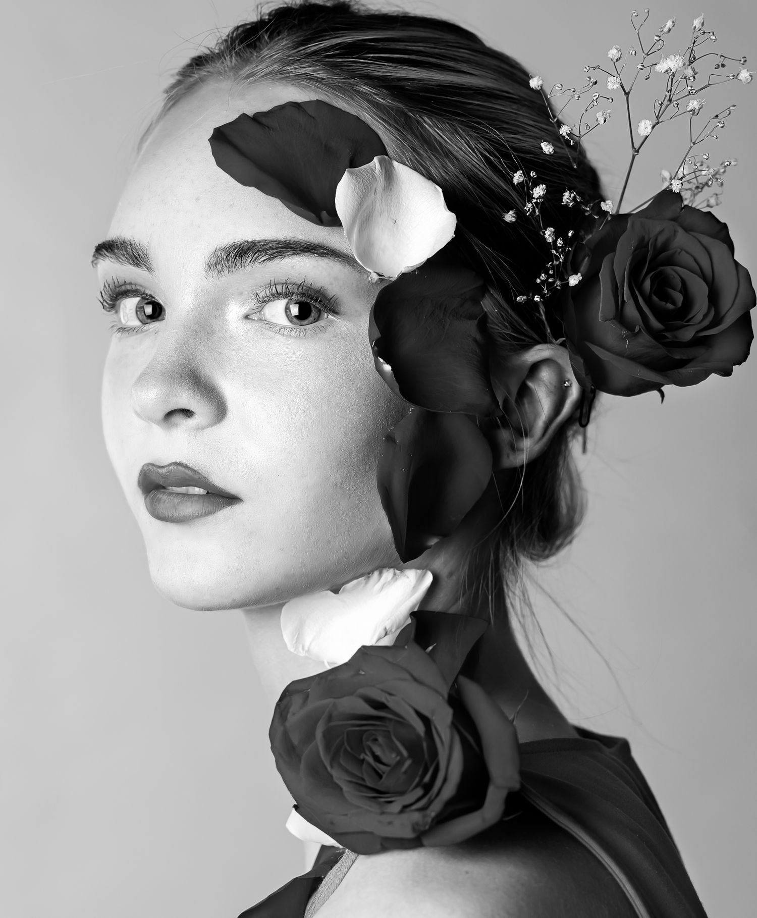 Black and white image of a girl looking at the camera with roses on her face and head