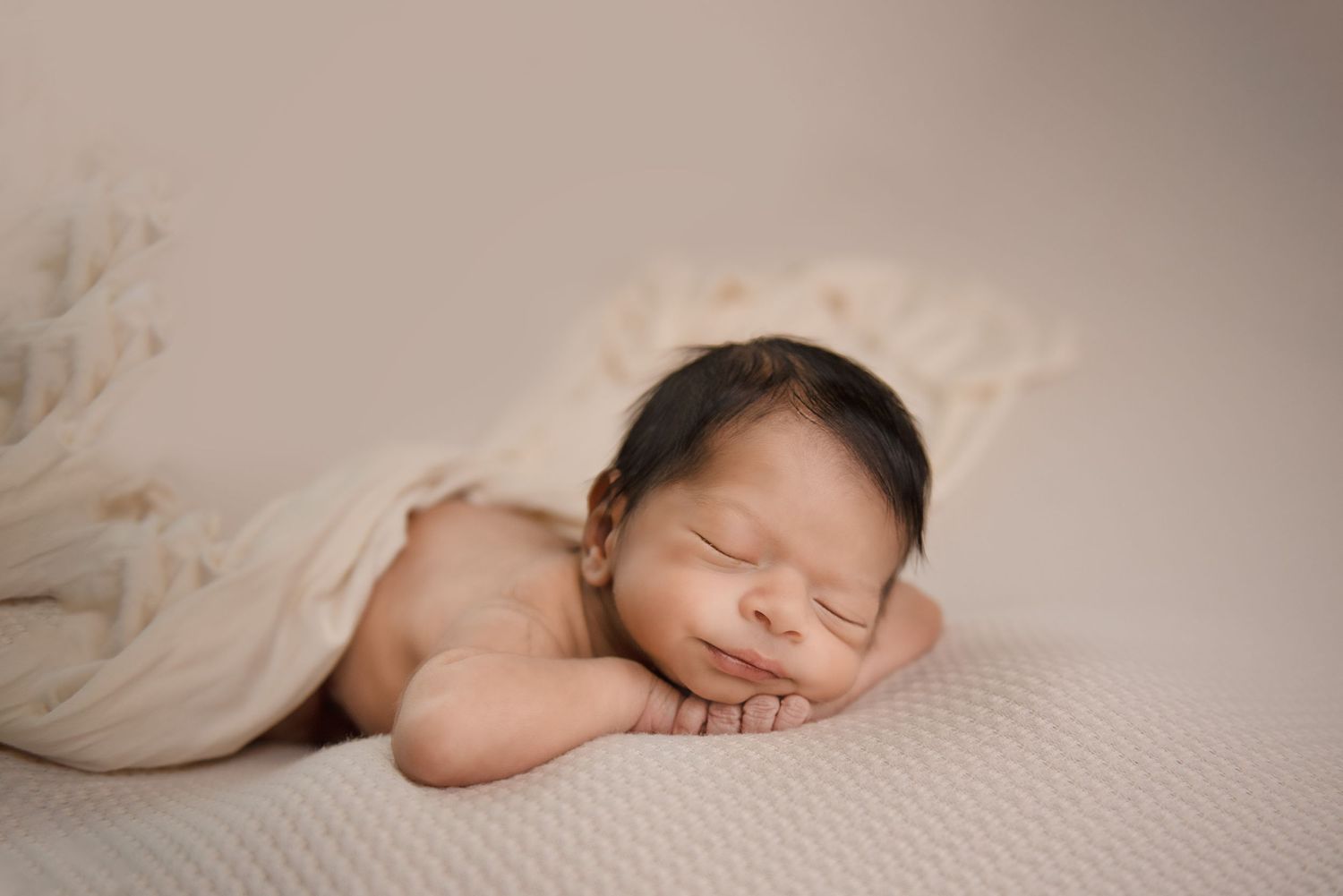 Peaceful newborn sleeping on textured cream blanket during portrait session.