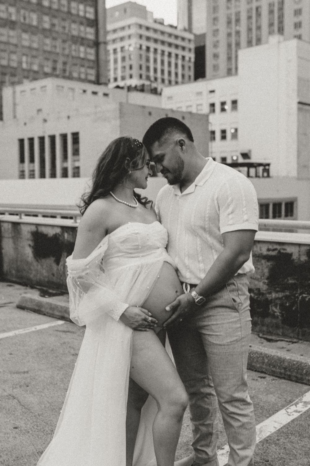 Black and white maternity photo of couple embracing on urban rooftop.