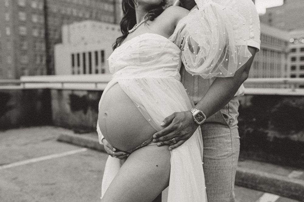 A black and white maternity photo captured on an urban rooftop with city buildings in the background.