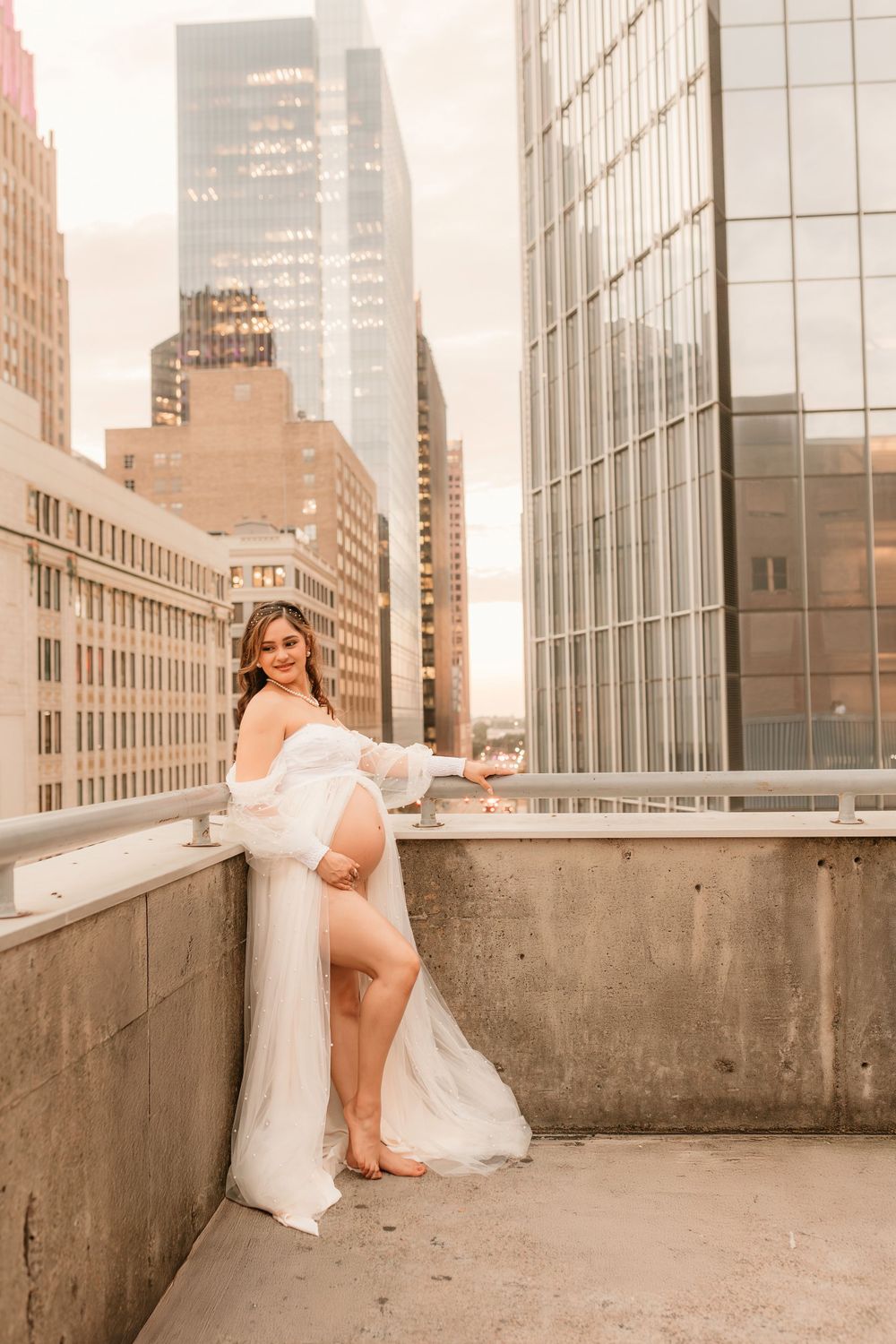 A maternity portrait featuring a flowing white dress against a cityscape backdrop.
