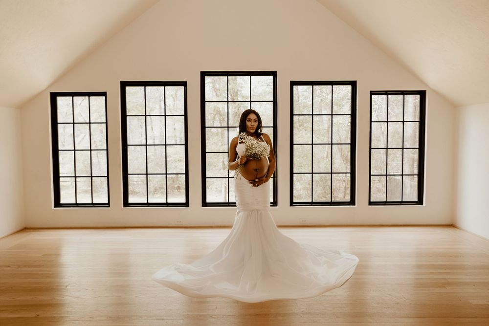 Bride in fitted mermaid wedding gown poses in front of large windows in bright room.