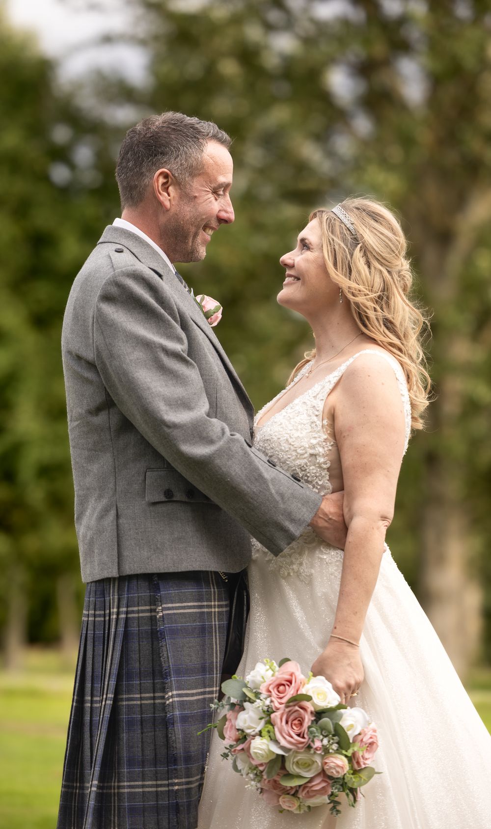 Happy bride and groom share joyful moments in traditional Scottish attire during their outdoor wedding celebration.