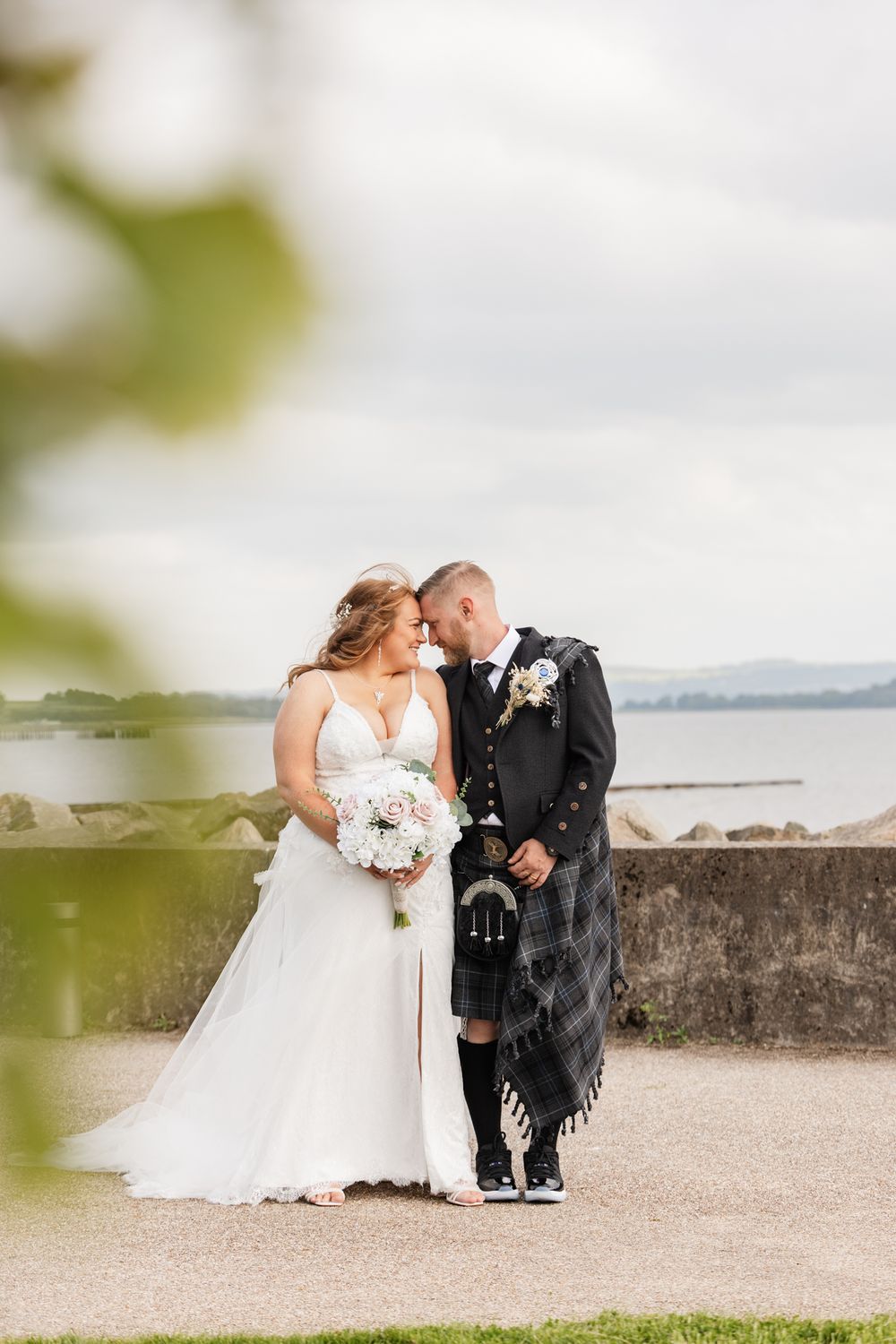 A romantic wedding couple shares intimate moments along a waterfront stone wall during their Scottish wedding photo session.