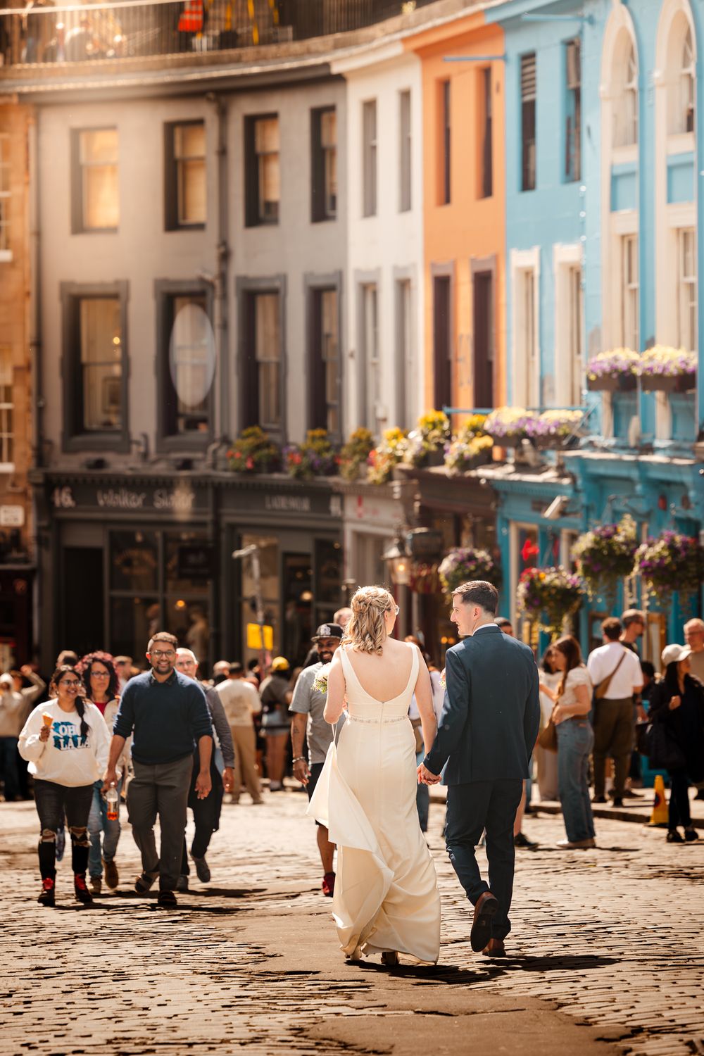 Couple walks down cobblestone street in historic shopping district with colorful pastel buildings and flower boxes.