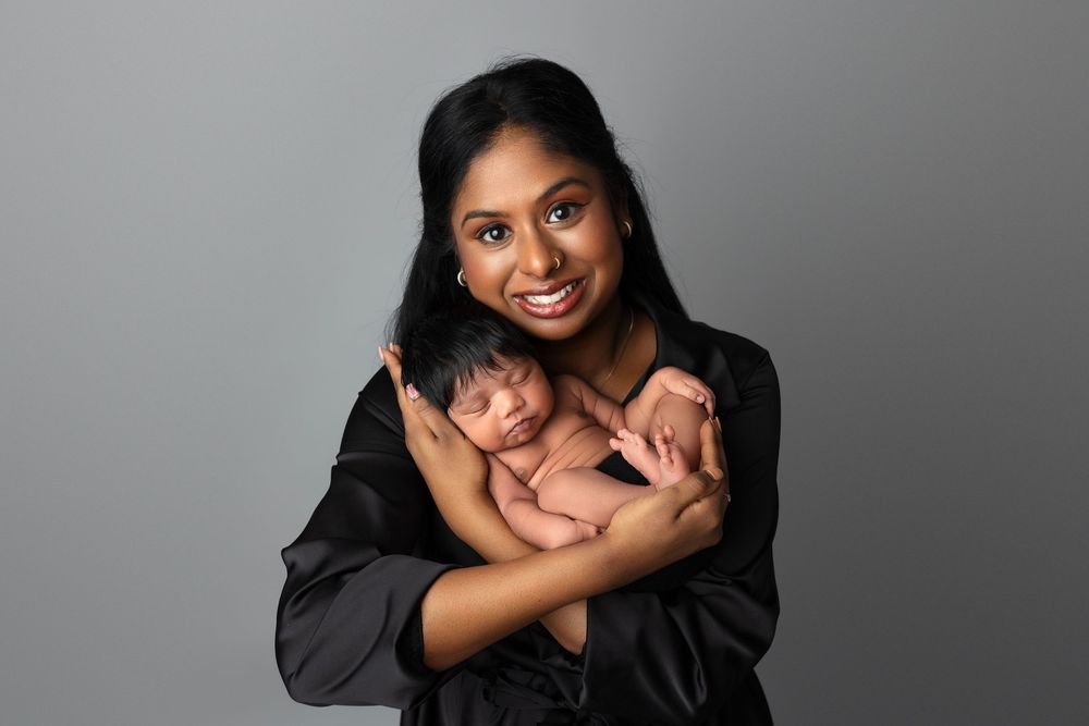 A family wearing black outfits poses together against a gray backdrop in a studio portrait session.