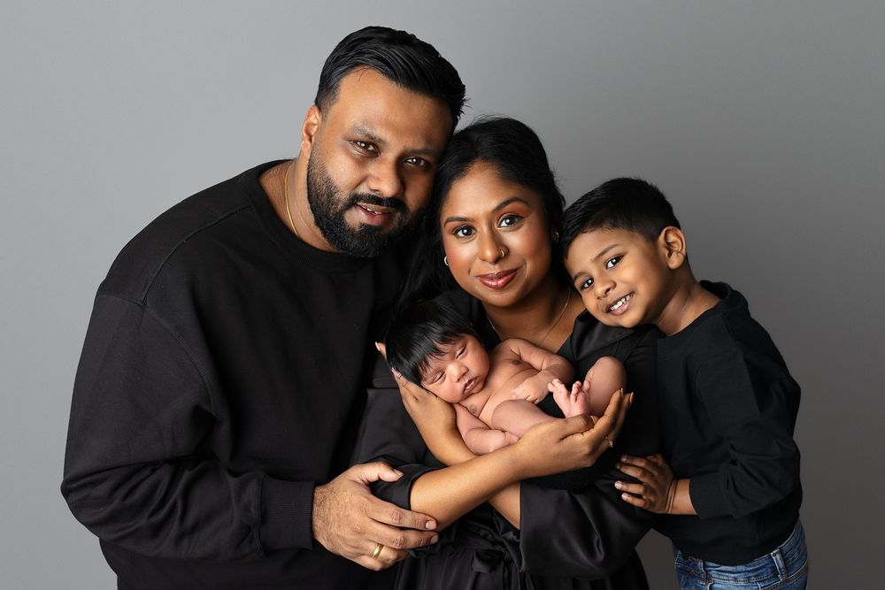 A family embraces warmly while dressed in coordinating black outfits during a professional photo shoot.