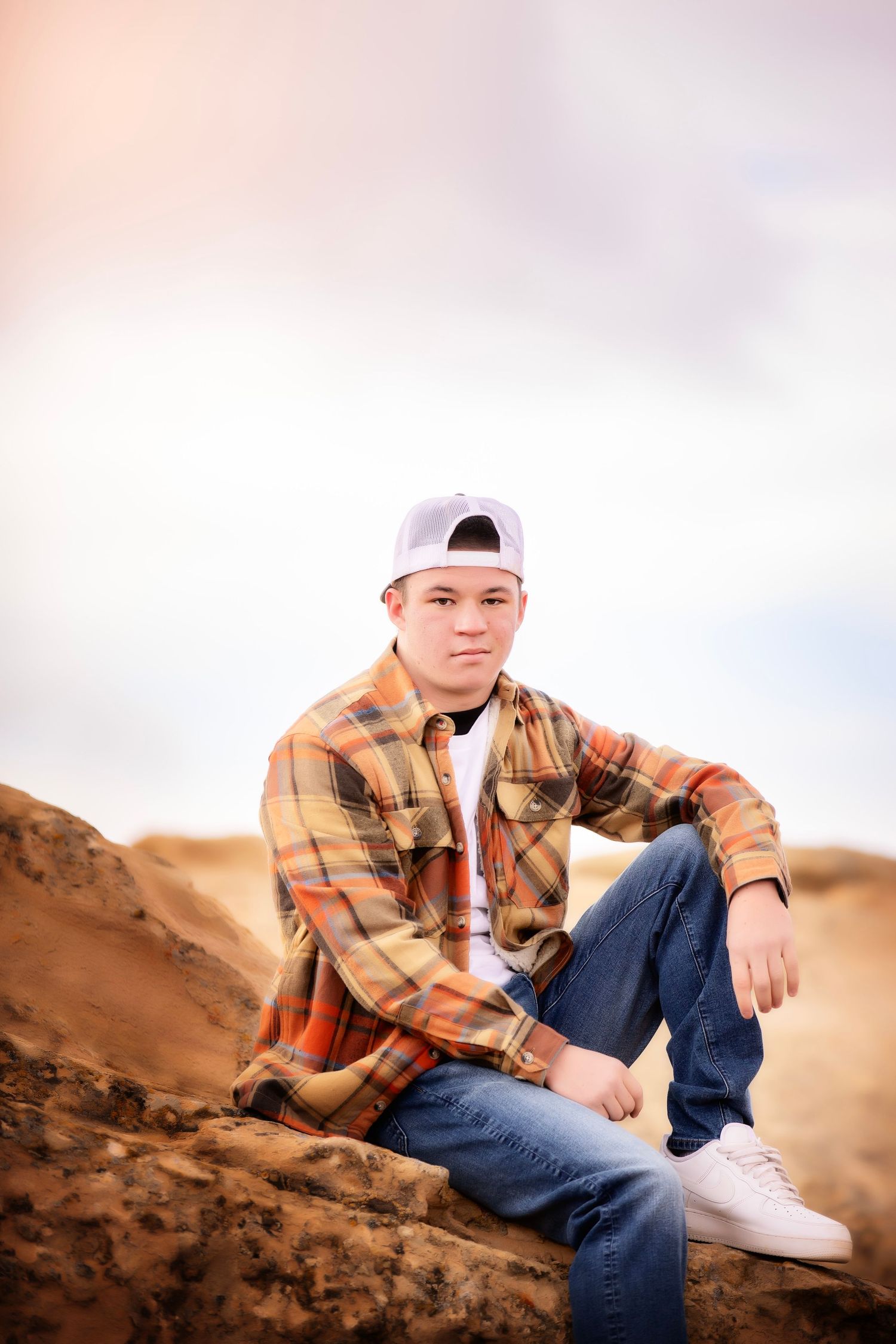 A casual portrait of someone in plaid flannel sitting on rocky terrain at sunset.