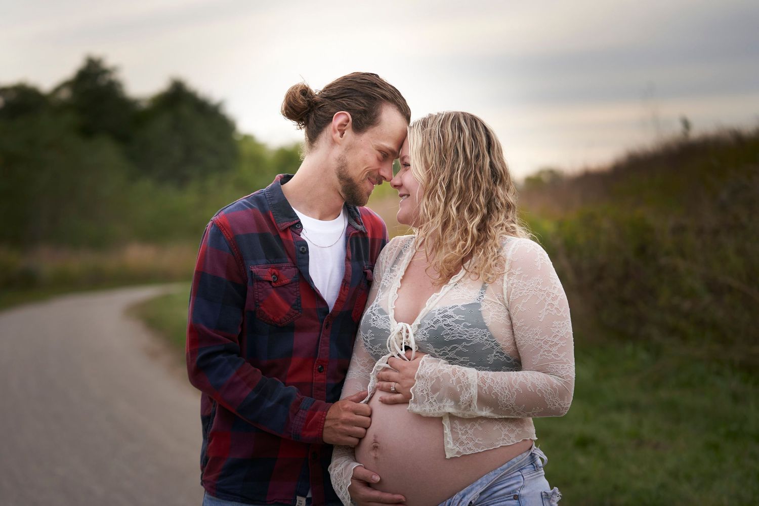 A tender maternity moment between a couple on a rural road during sunset, with the mother-to-be wearing lace.